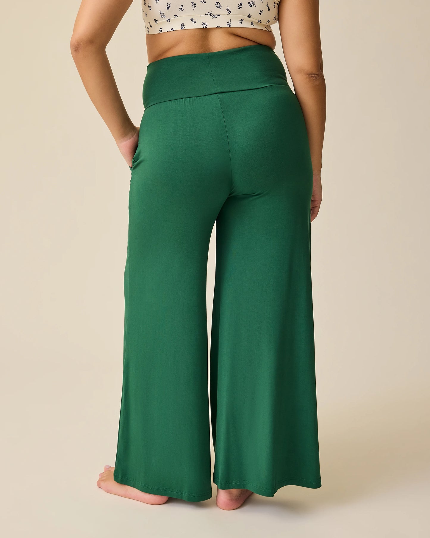 Back view of model wearing Bamboo Wide Leg Maternity & Postpartum Lounge Pant in Deep Green on a beige background. 