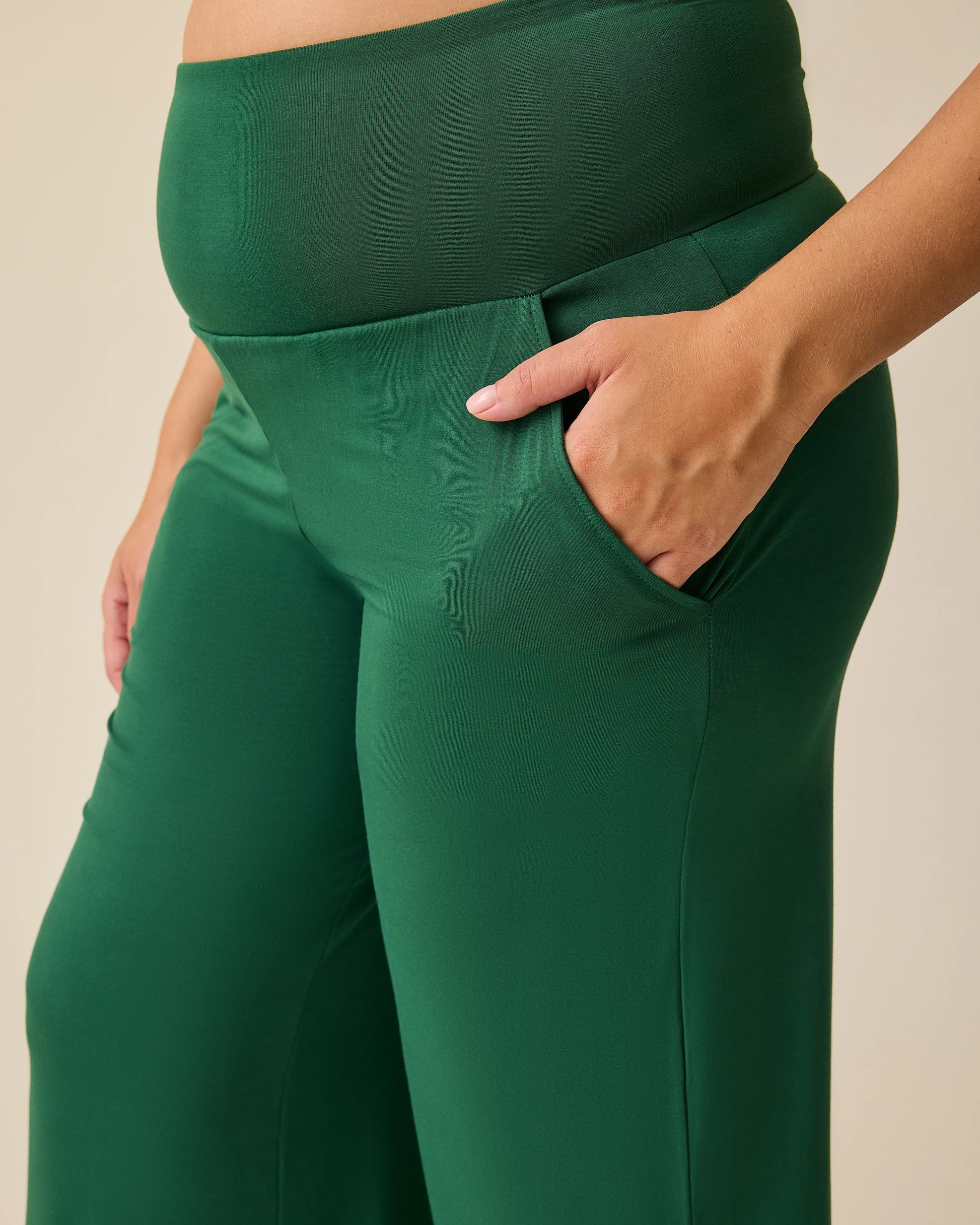 Side view of waist of model wearing Bamboo Wide Leg Maternity & Postpartum Lounge Pant in Deep Green on a beige background. 