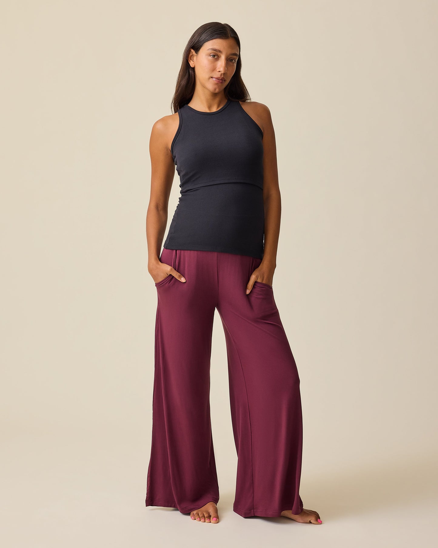 Model is wearing Bamboo Wide Leg Maternity & Postpartum Lounge Pant in Fig and Ribbed Bamboo Racerback Nursing Tank in Black on a beige background. @model_info:Hayley is 5'7" and wearing a Small.