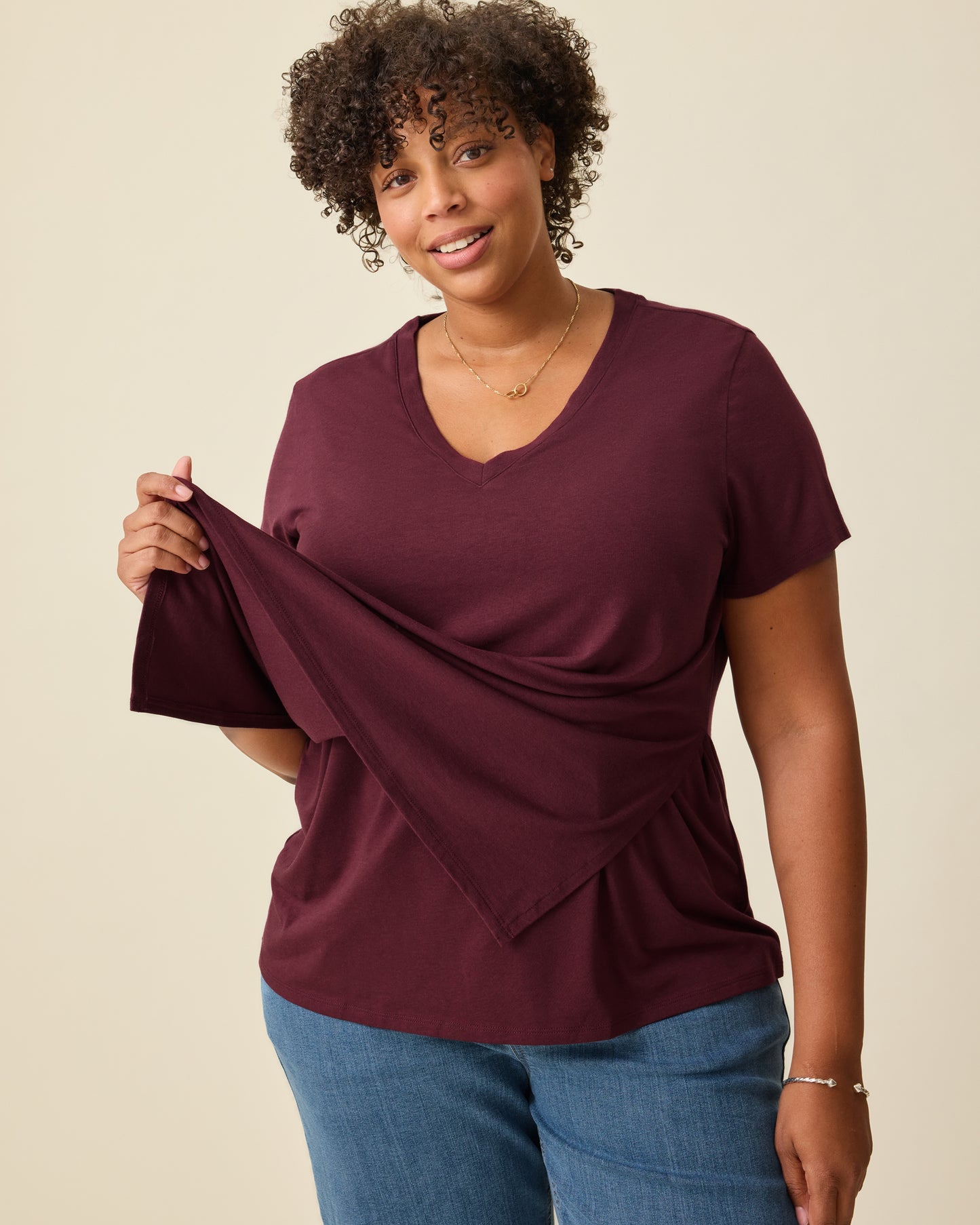 Model is displaying the front panel lift-up for breastfeeding access on the Modal V-neck Nursing T-shirt in Deep Burgundy on a beige background. 