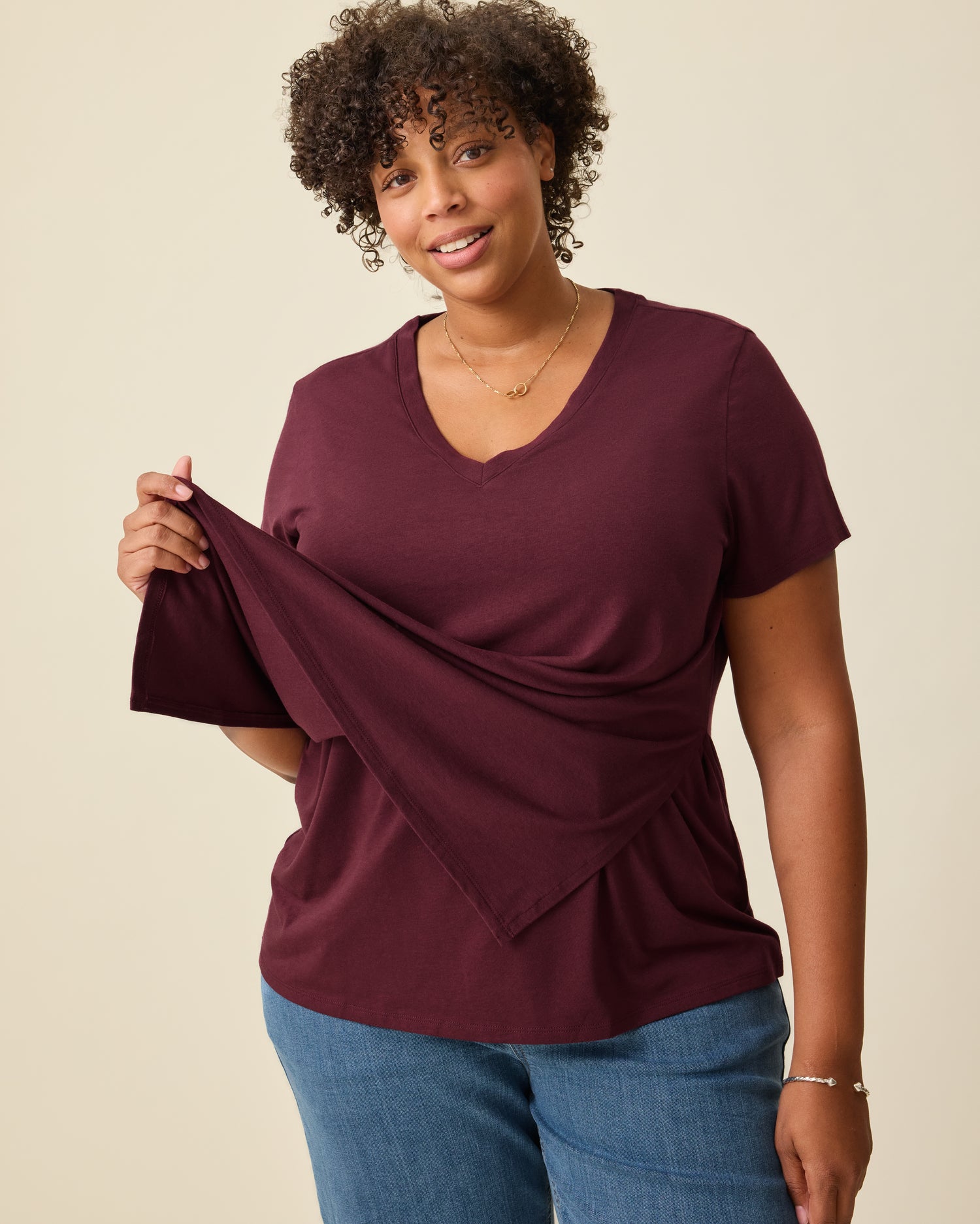 Model is displaying the front panel lift-up for breastfeeding access on the Modal V-neck Nursing T-shirt in Deep Burgundy on a beige background. 