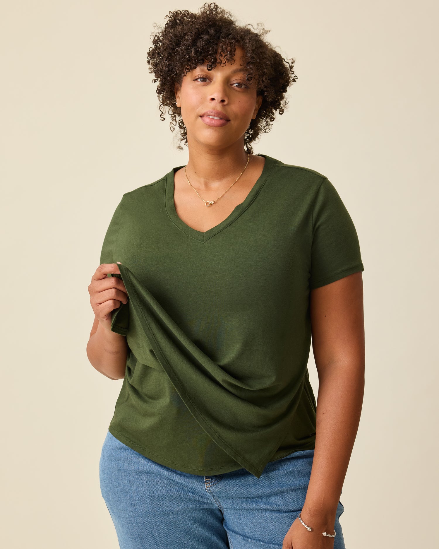 Model is lifting up the front panel to show breastfeeding access on the Modal V-neck Nursing T-shirt in Deep Olive on a beige background.