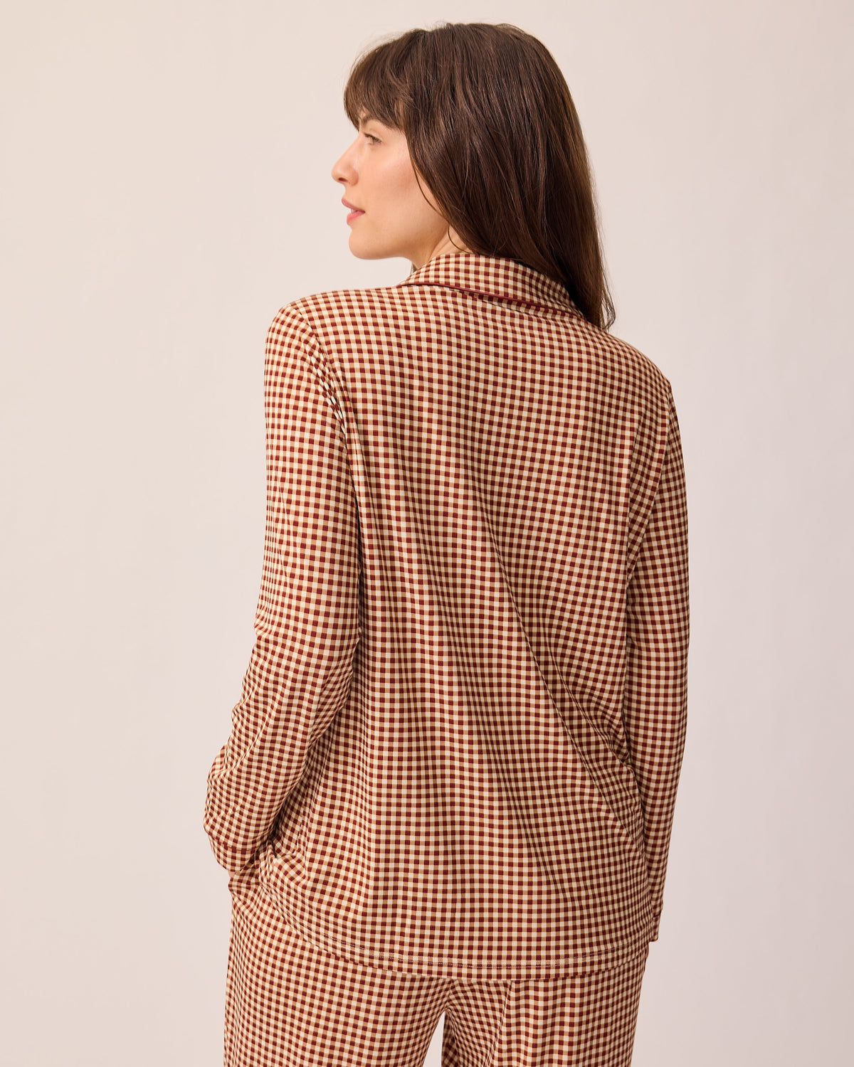 Back view of model wearing Clea Bamboo Long Sleeve Pajama Set in Auburn Gingham, on a beige background.