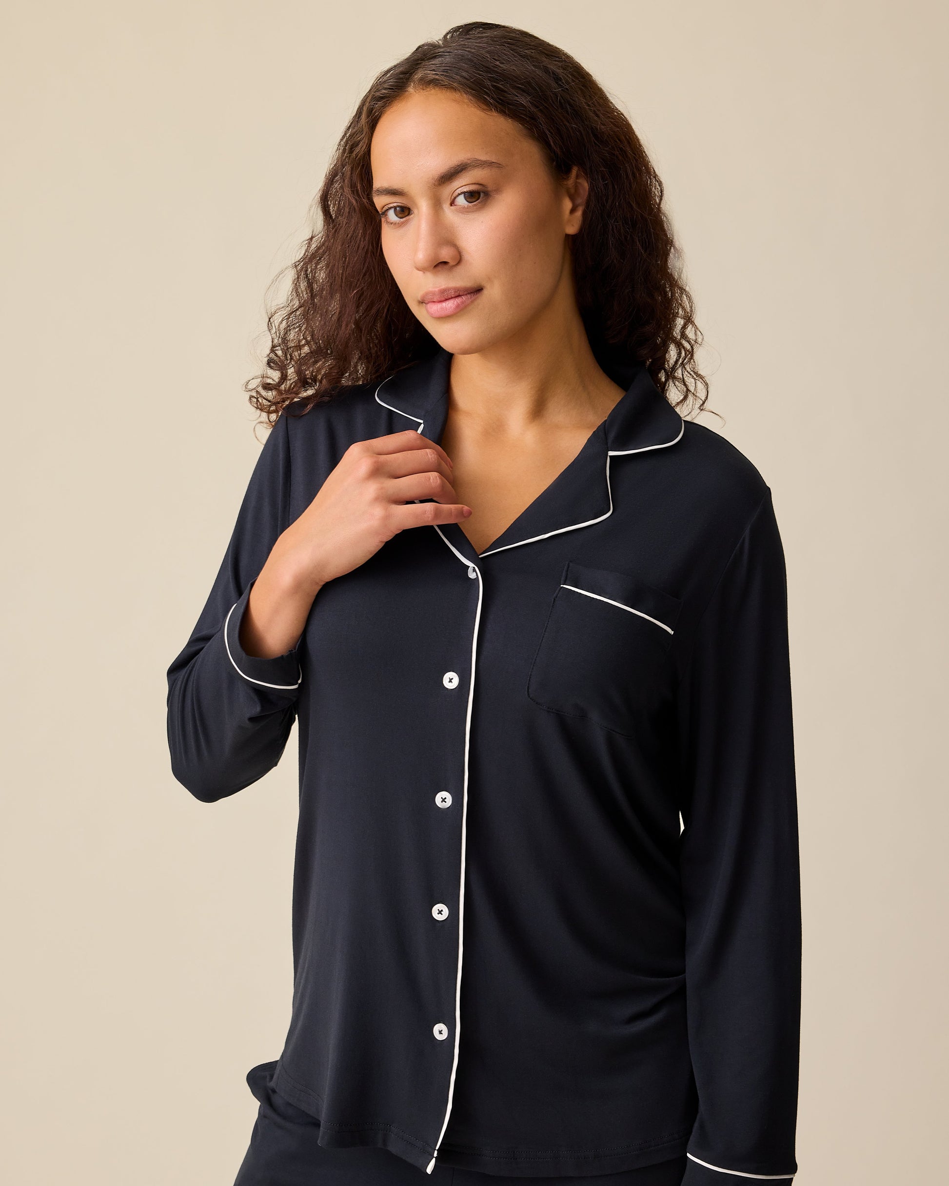 Close up of model wearing Clea Bamboo Long Sleeve Pajama Set in Black on a beige background. 
