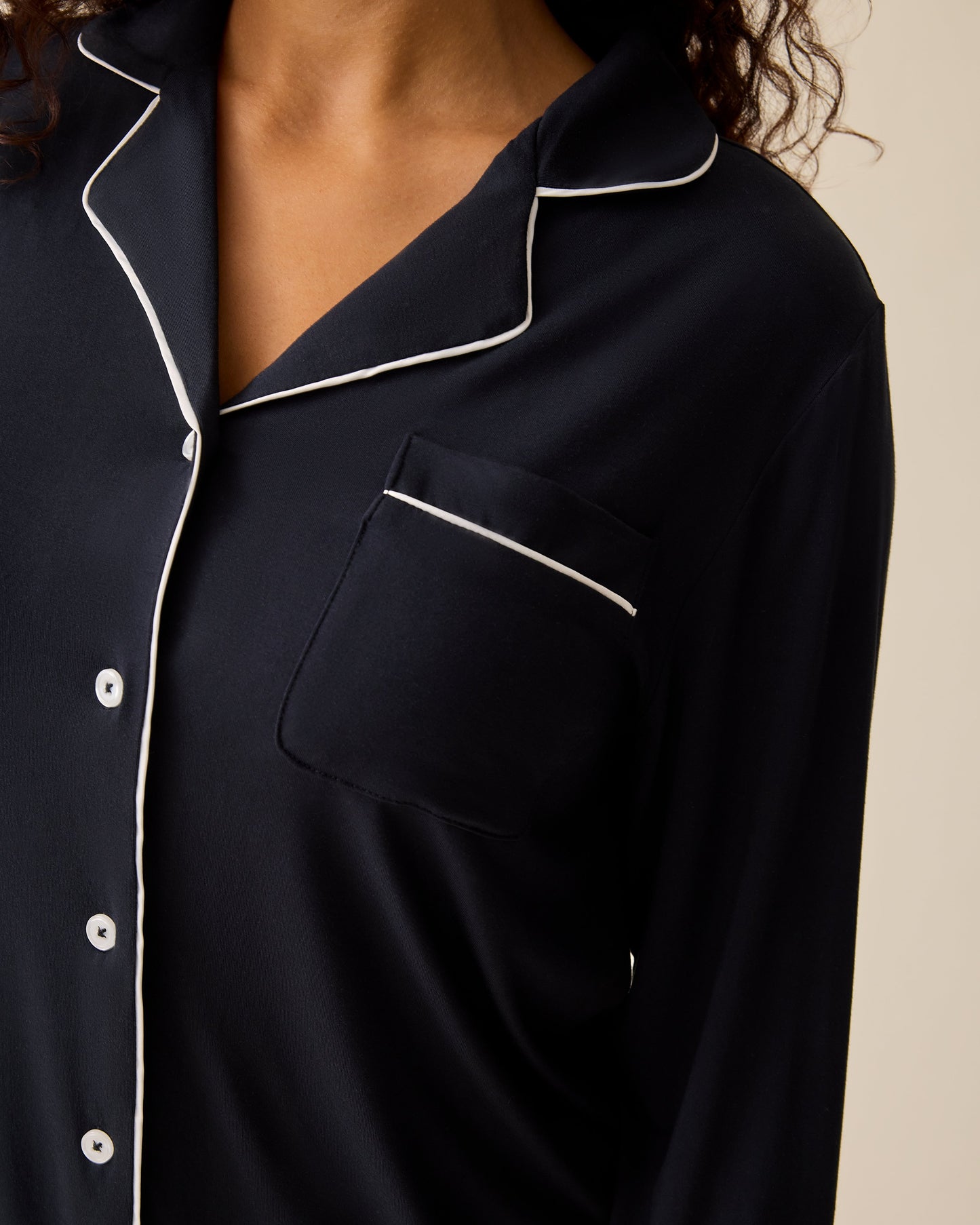 Close up of model wearing Clea Bamboo Long Sleeve Pajama Set in Black on a beige background. 