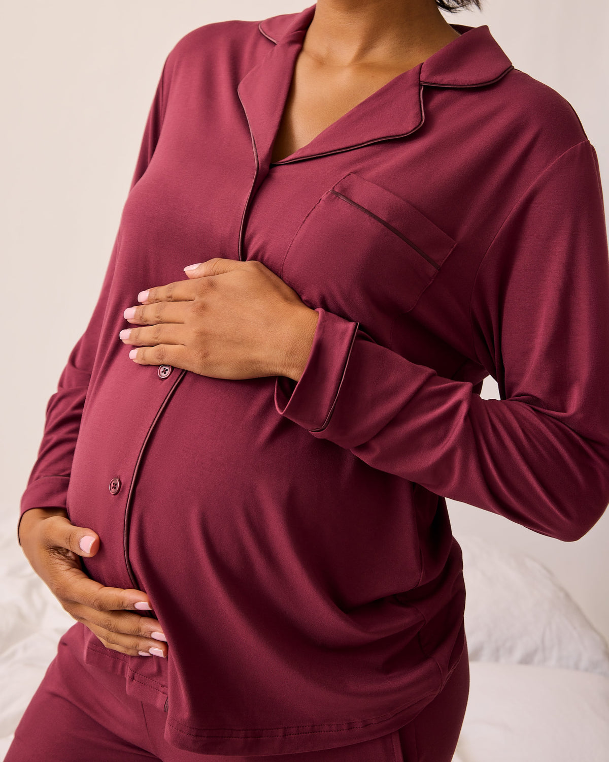 Angled view of model wearing Clea Bamboo Long Sleeve Pajama Set in Deep Burgundy on a beige background.