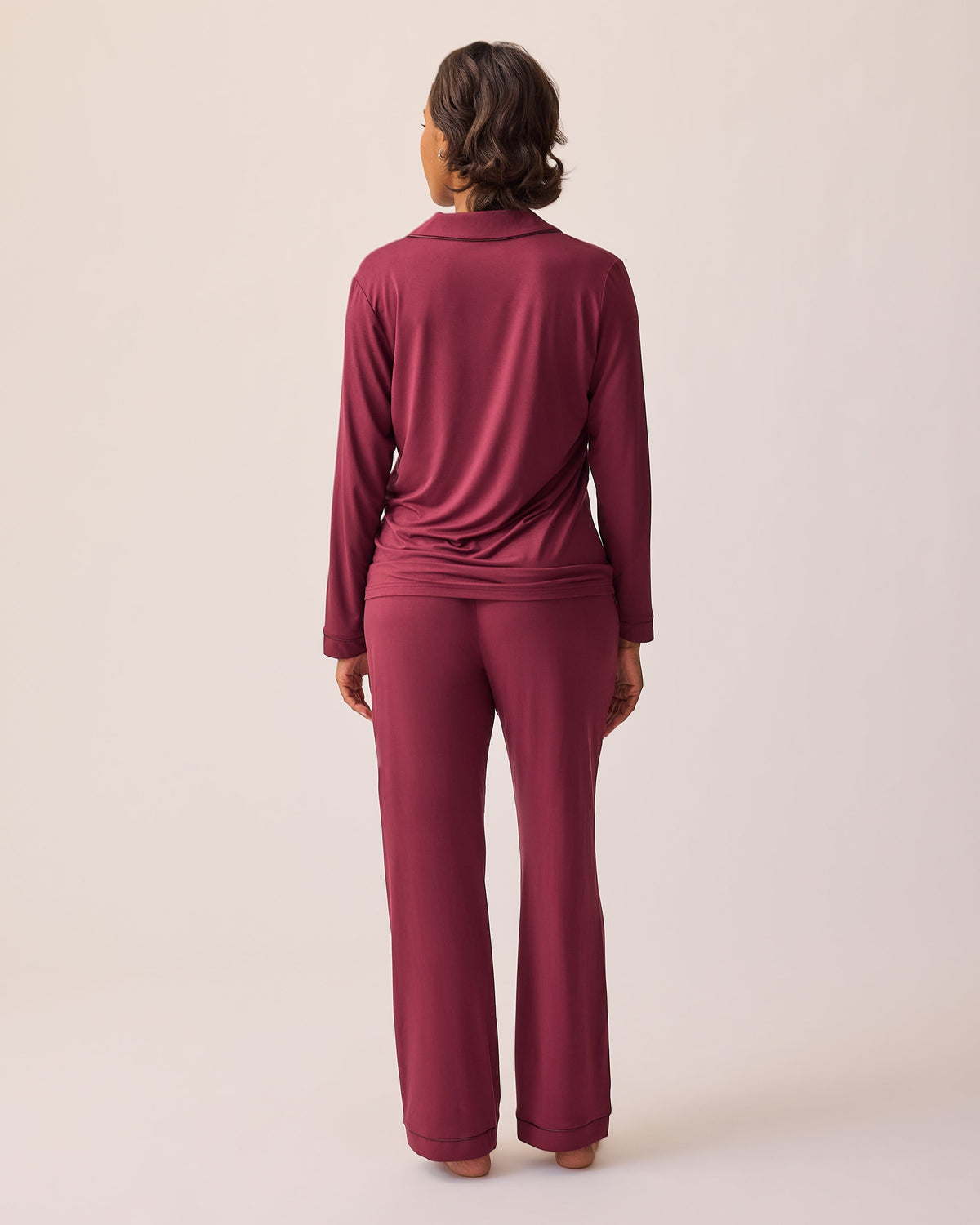 Back view of model wearing Clea Bamboo Long Sleeve Pajama Set in Deep Burgundy on a beige background.