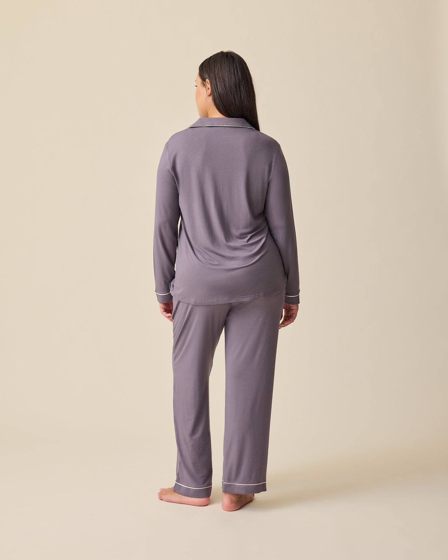 Back view of the model wearing the Clea Bamboo Long Sleeve Pajama Set in Granite on a beige background. 