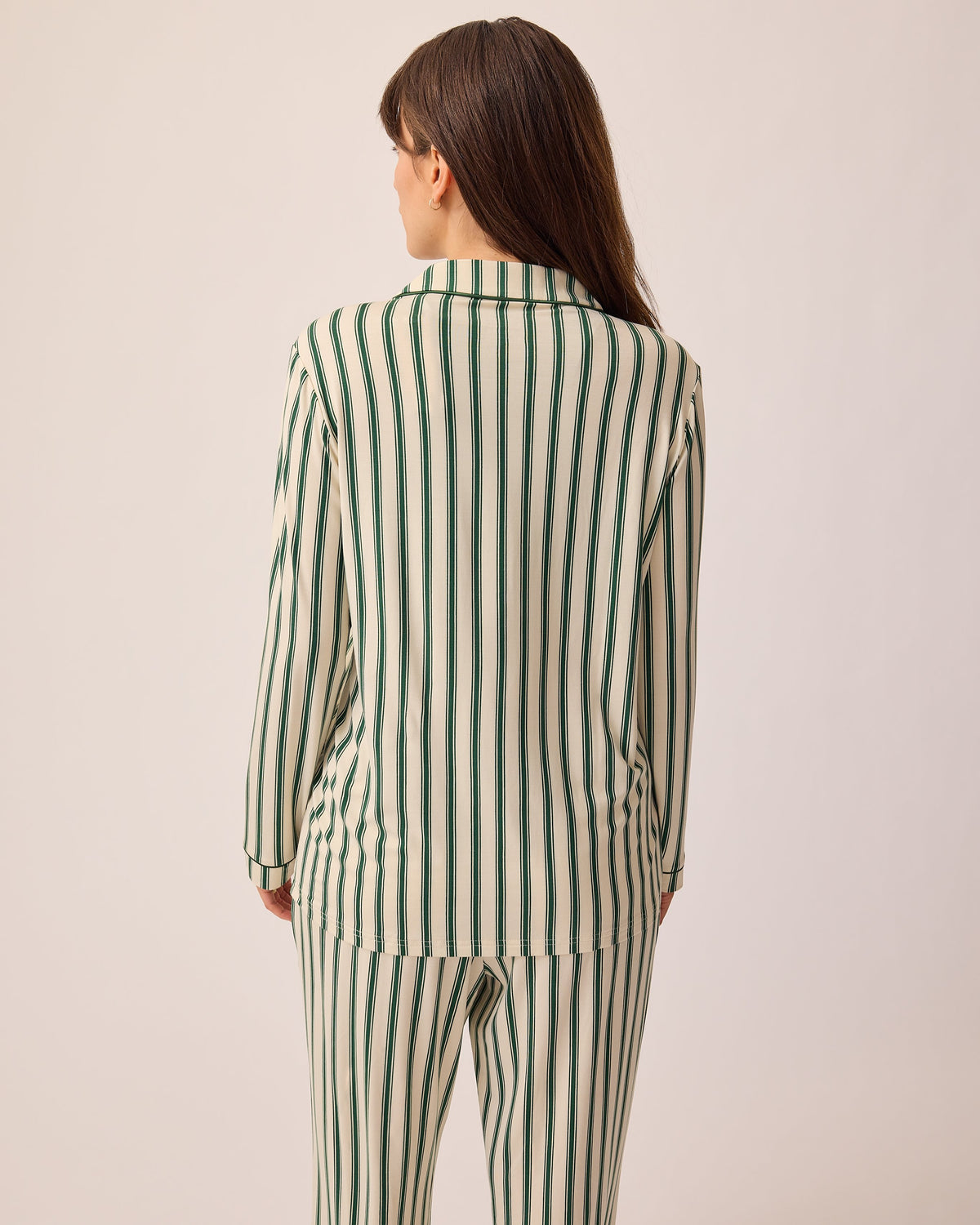 Back view of model wearing Clea Bamboo Long Sleeve Pajama Set in Green Candy Stripe, on a beige background.