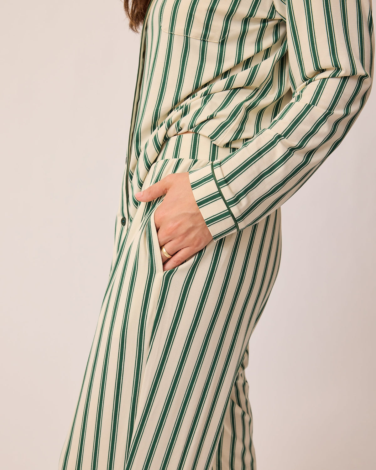 Side view of model wearing Clea Bamboo Long Sleeve Pajama Set in Green Candy Stripe, on a beige background.