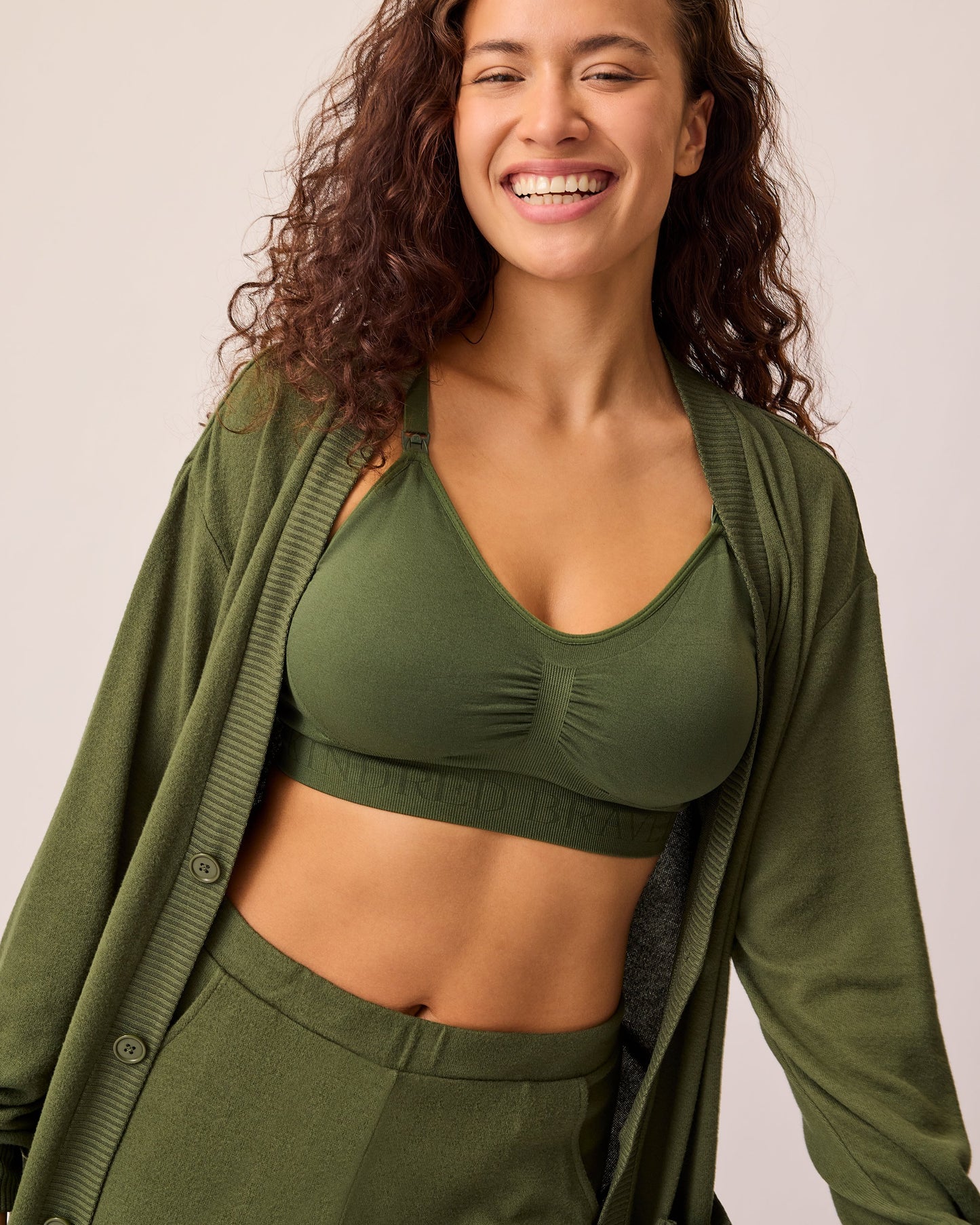 Model is wearing CozyKnit Long Cardigan in Deep Olive unbuttoned, with Simply Sublime® Nursing Bra in Deep Olive, and CozyKnit Wide Leg Lounge Pant in Deep Olive on a beige background.