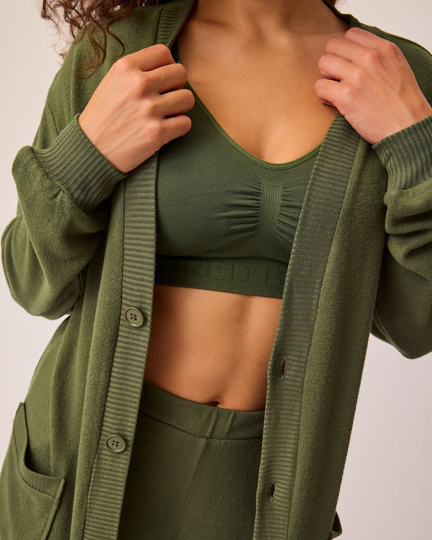 Model is wearing CozyKnit Long Cardigan in Deep Olive unbuttoned, with Simply Sublime® Nursing Bra in Deep Olive, and CozyKnit Wide Leg Lounge Pant in Deep Olive on a beige background.
