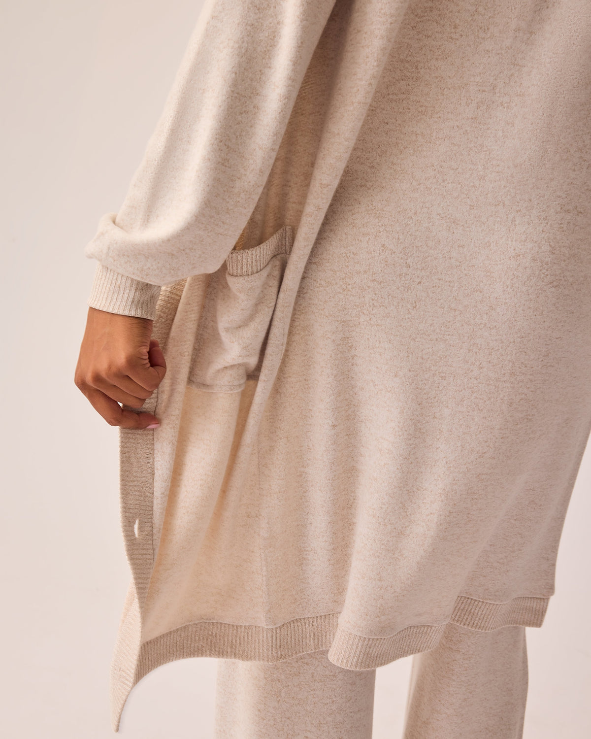 Back view of model wearing CozyKnit Wide Leg Lounge Pant in Oat, and CozyKnit Long Cardigan in Oat, on a beige background.