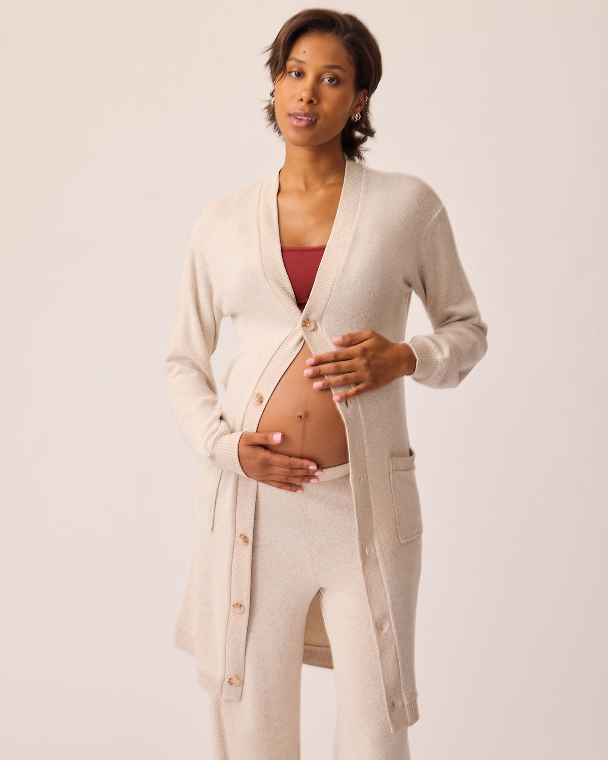 Model is wearing CozyKnit Wide Leg Lounge Pant in Oat, and CozyKnit Long Cardigan in Oat, and French Terry Maternity & Nursing Bralette in Deep Burgundy on a beige background.
@model_info:Ale is 5'9" and wearing a Small.