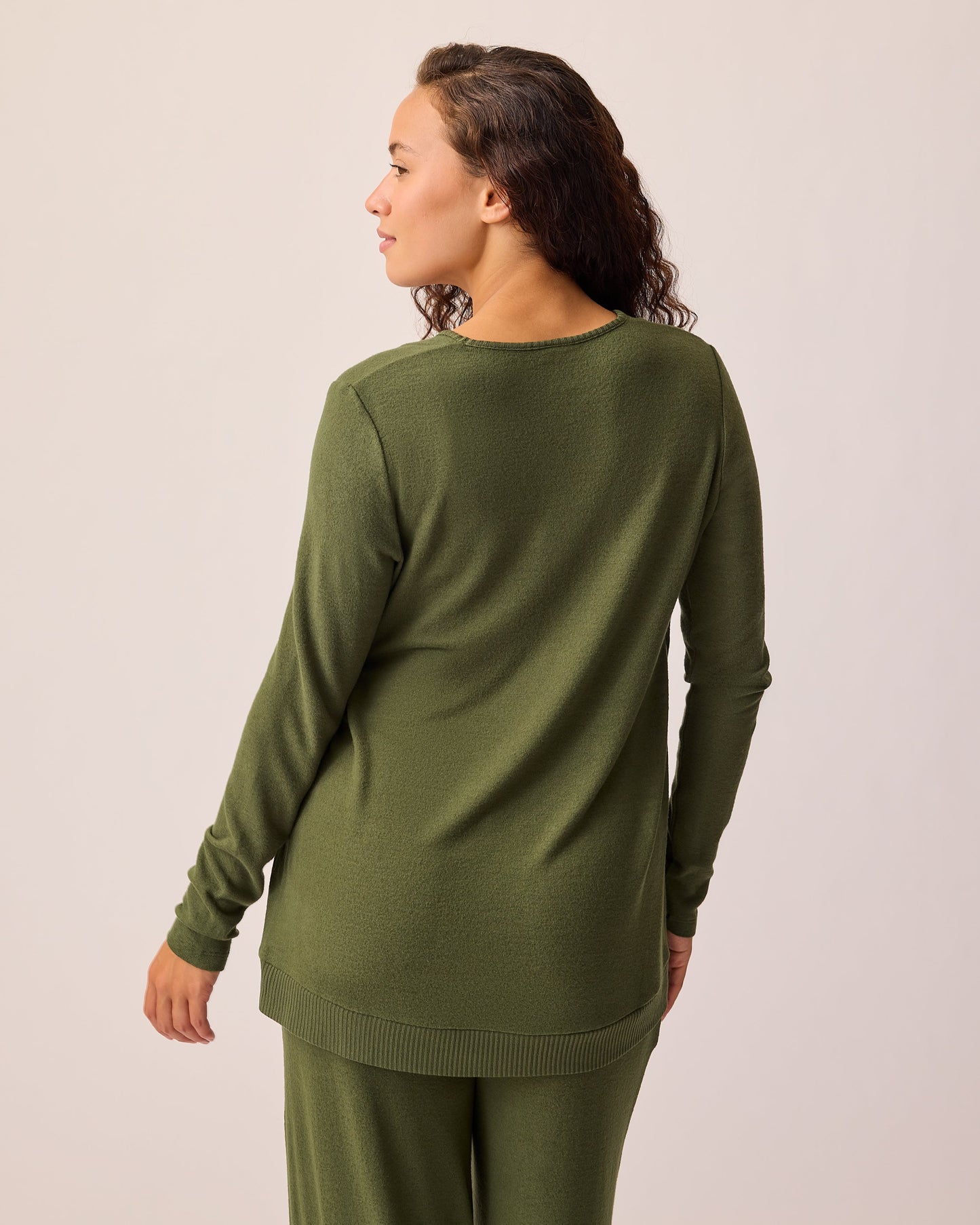 Back view of model wearing CozyKnit Maternity & Nursing V-neck Top in Deep Olive on a beige background. 