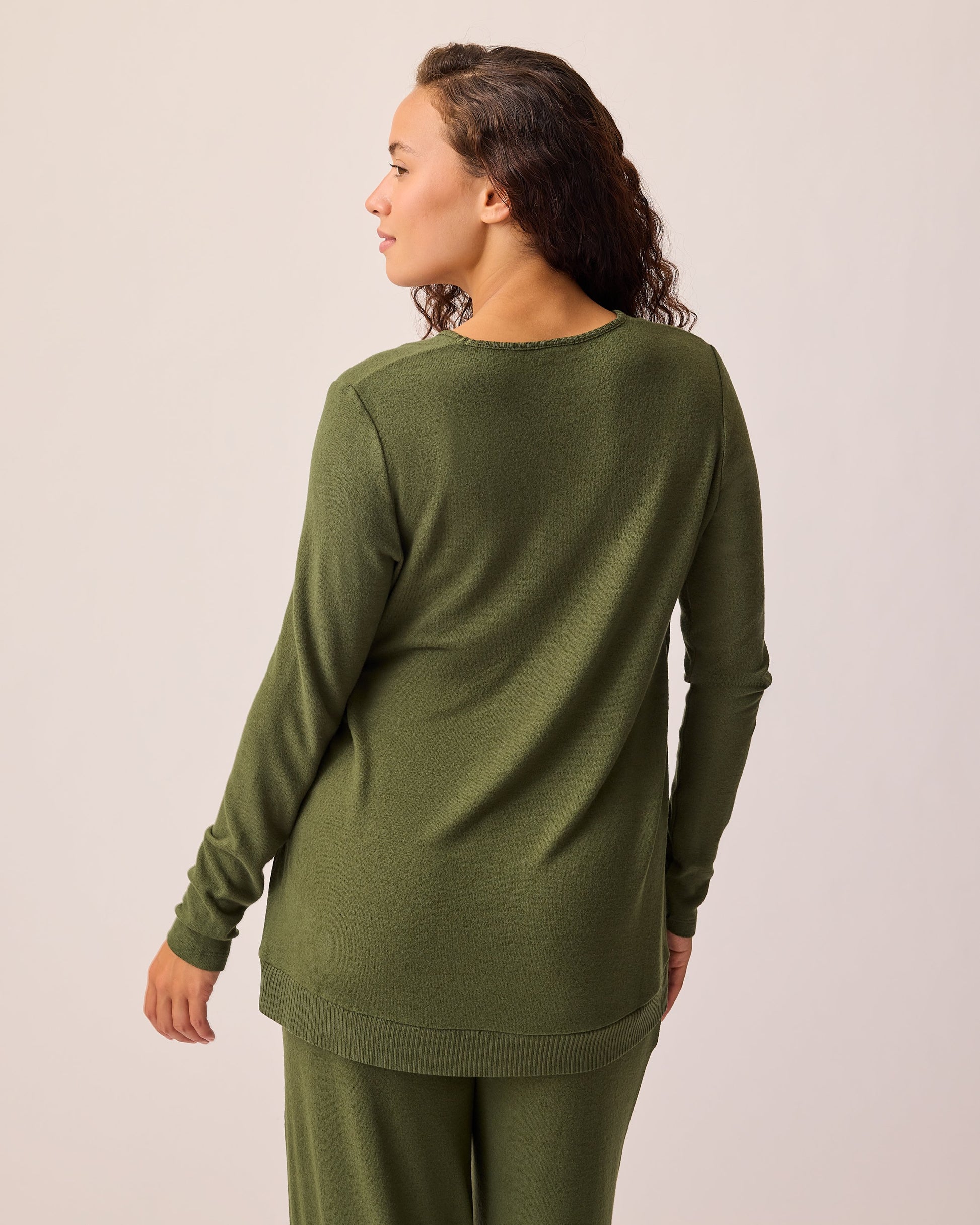 Back view of model wearing CozyKnit Maternity & Nursing V-neck Top in Deep Olive on a beige background. 