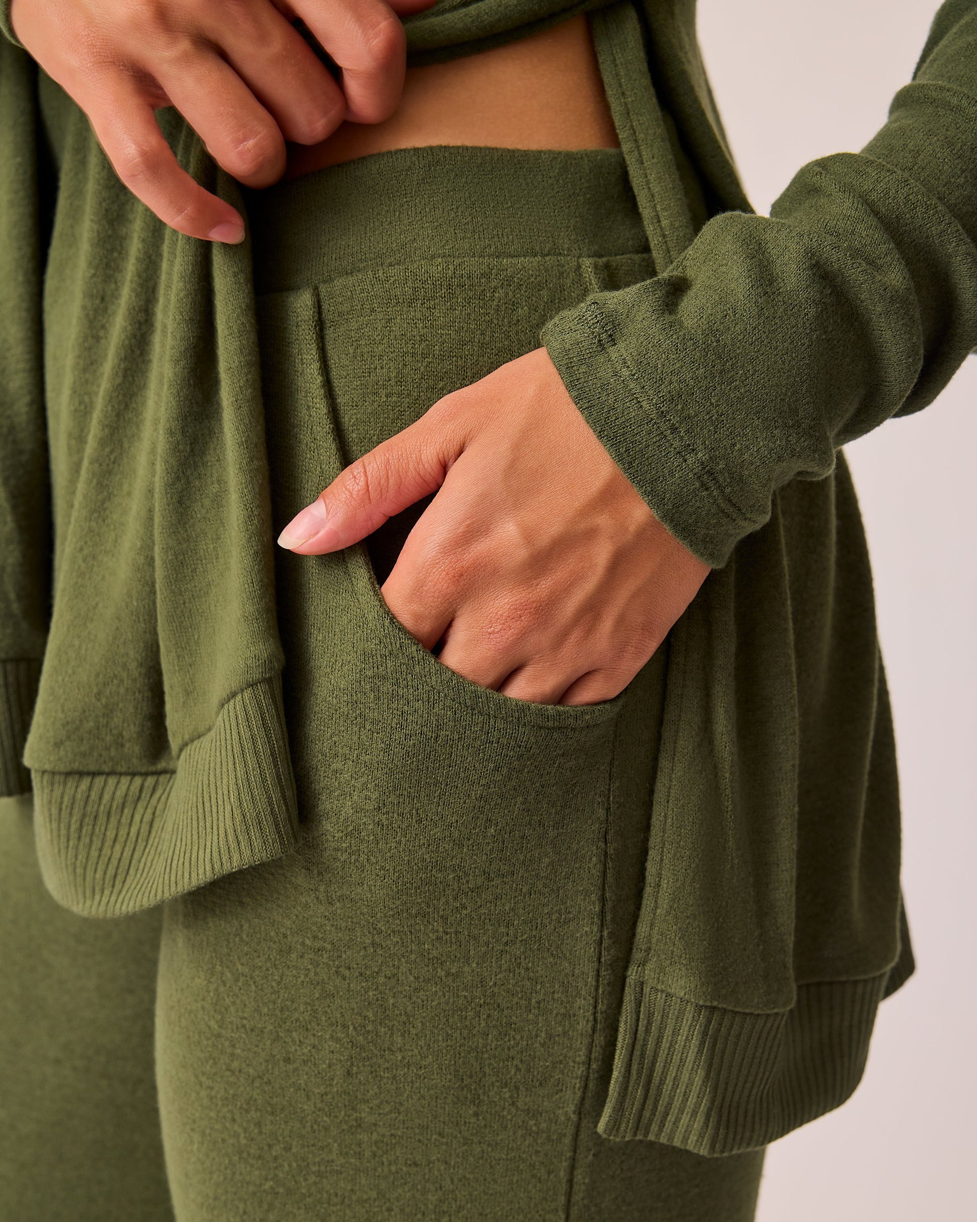 Close up of pockets on CozyKnit Wide Leg Lounge Pant in Deep Olive on a beige background.