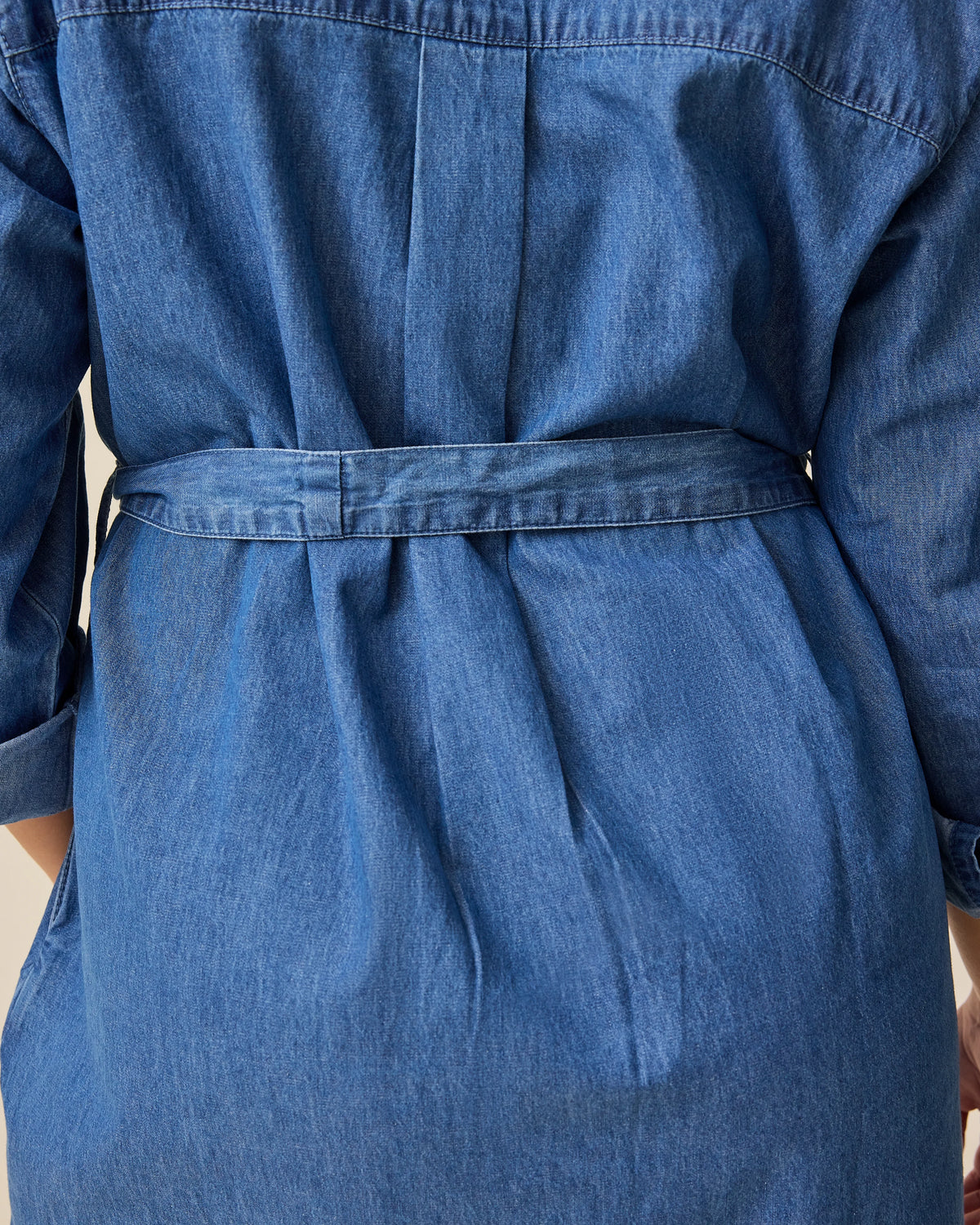 Back view of model wearing Denim Maternity & Nursing Shirt Dress in Dark Wash and close up of denim belt, on a beige background.