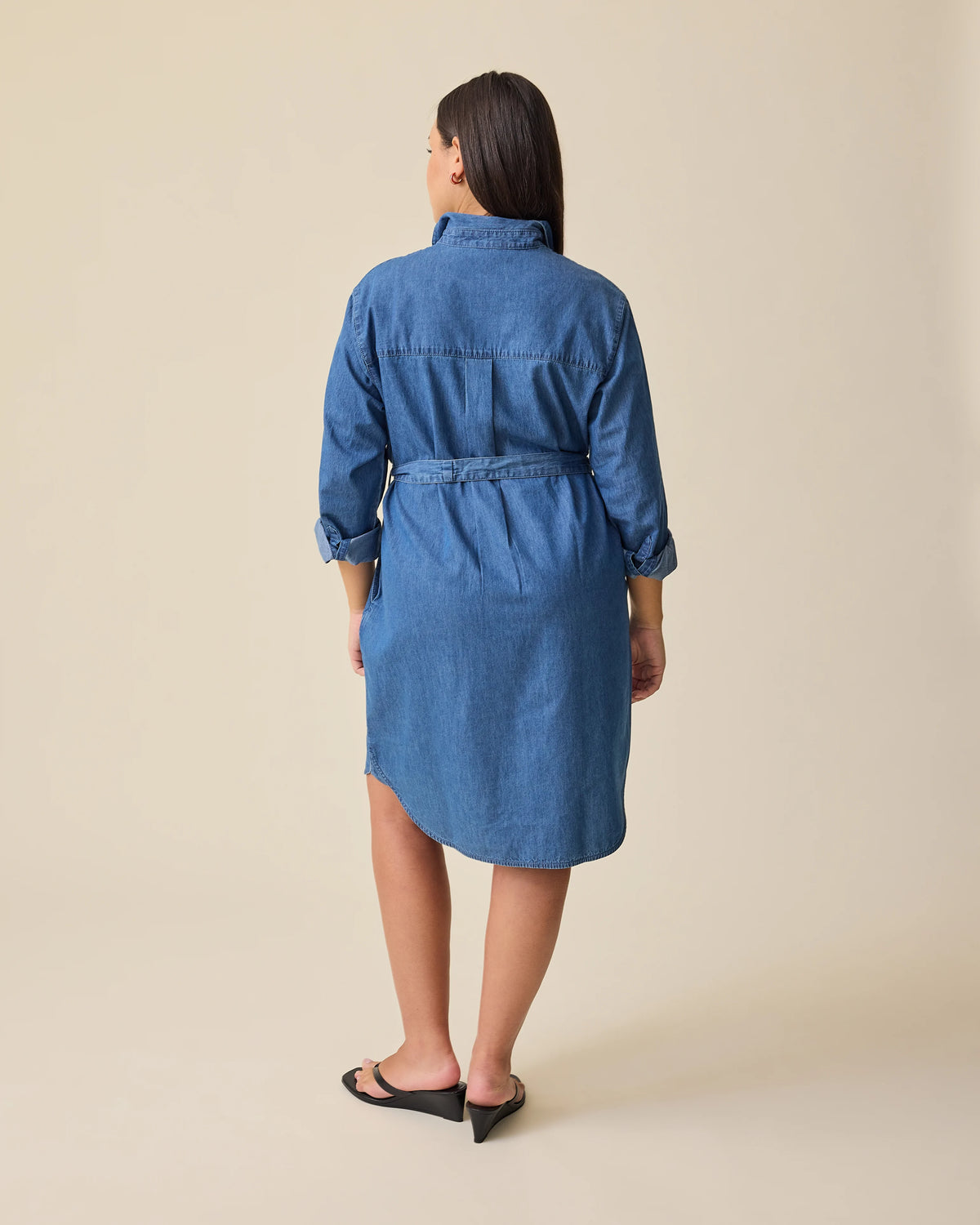 Back view of model wearing Denim Maternity & Nursing Shirt Dress in Dark Wash on a beige background.