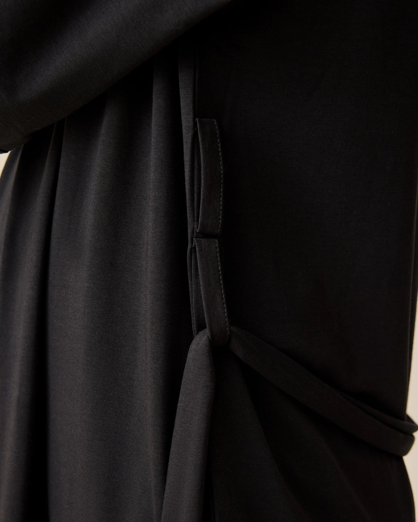 Side view of model wearing The Restore Cotton Blend Robe in Black on a beige background.