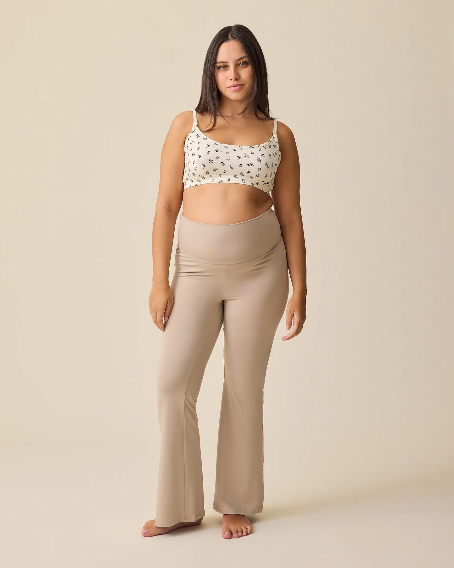 Front view of model wearing French Terry Racerback Nursing & Sleep Bra in Ivory Wildflower and Bamboo Flex Maternity & Postpartum Flare Pant in Sandstone with the waist unfolded on a beige background.