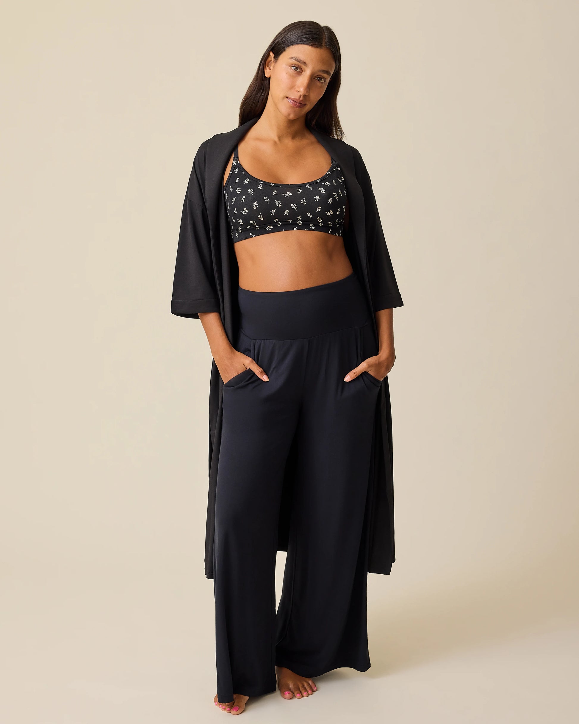 Model is wearing The Restore Cotton Blend Robe in Black and French Terry Racerback Nursing & Sleep Bra in Black Wildflower on a beige background.