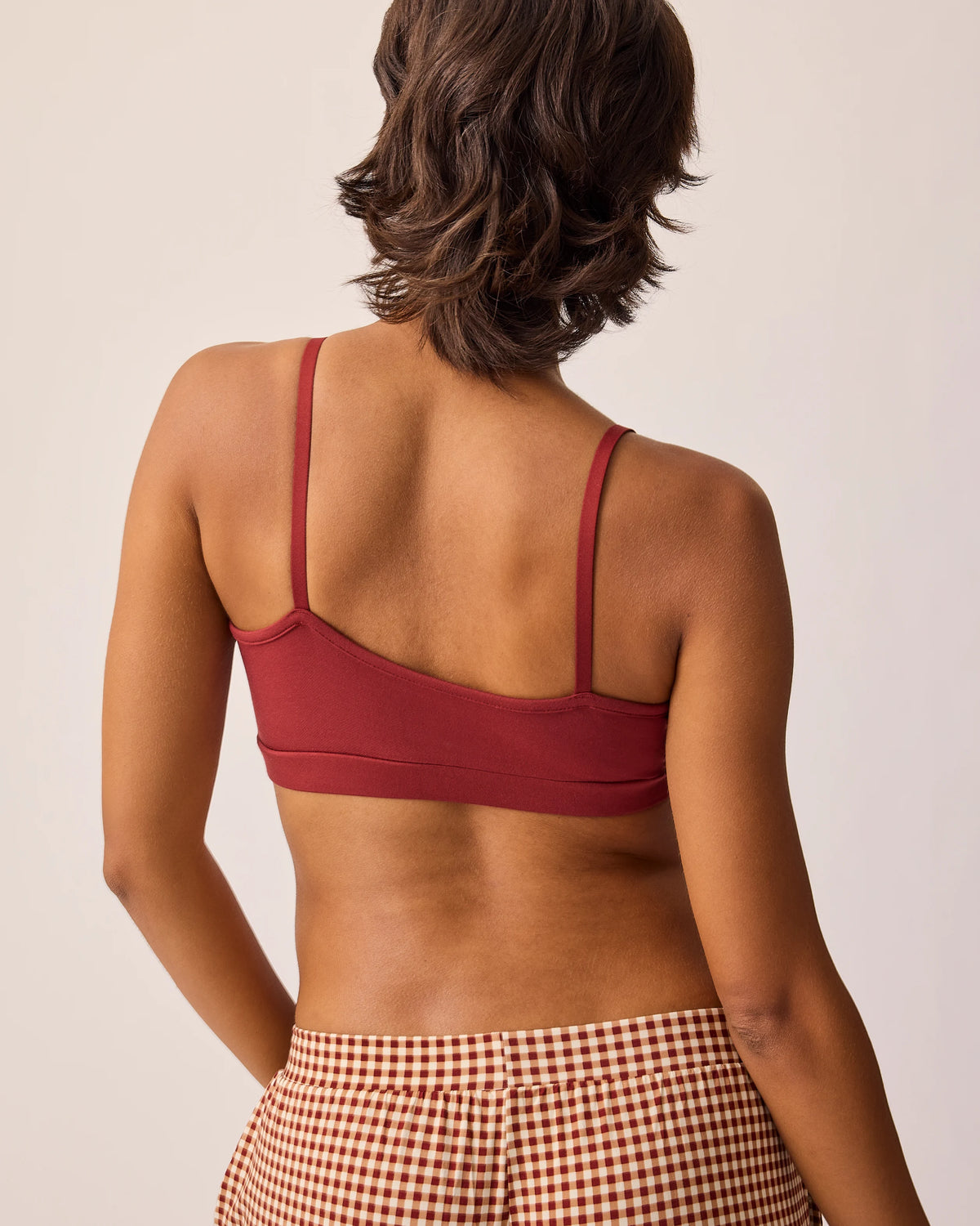 Back view of model wearing the French Terry Maternity & Nursing Bralette in Auburn and Clea Bamboo Long Sleeve Pajama Pant in Auburn Gingham, on a beige background. 