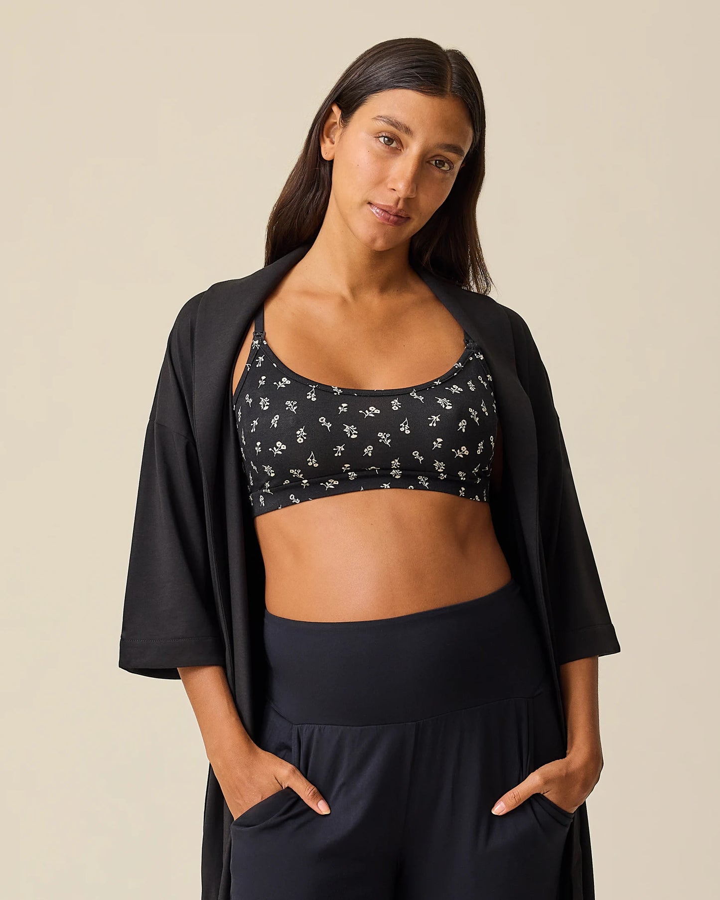 Model is wearing The Restore Cotton Blend Robe in Black and French Terry Maternity & Nursing Bralette in Black Wildflower on a beige background.