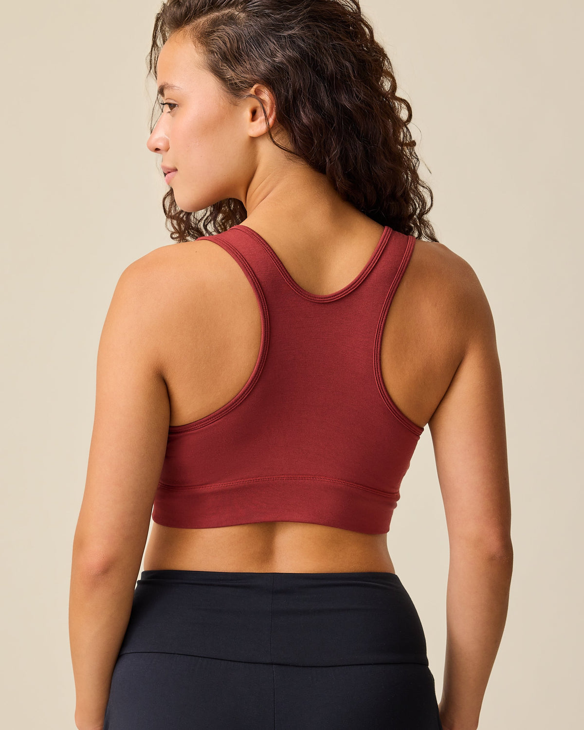 Back view of model wearing French Terry Racerback Nursing & Sleep Bra in Auburn on a beige background. 