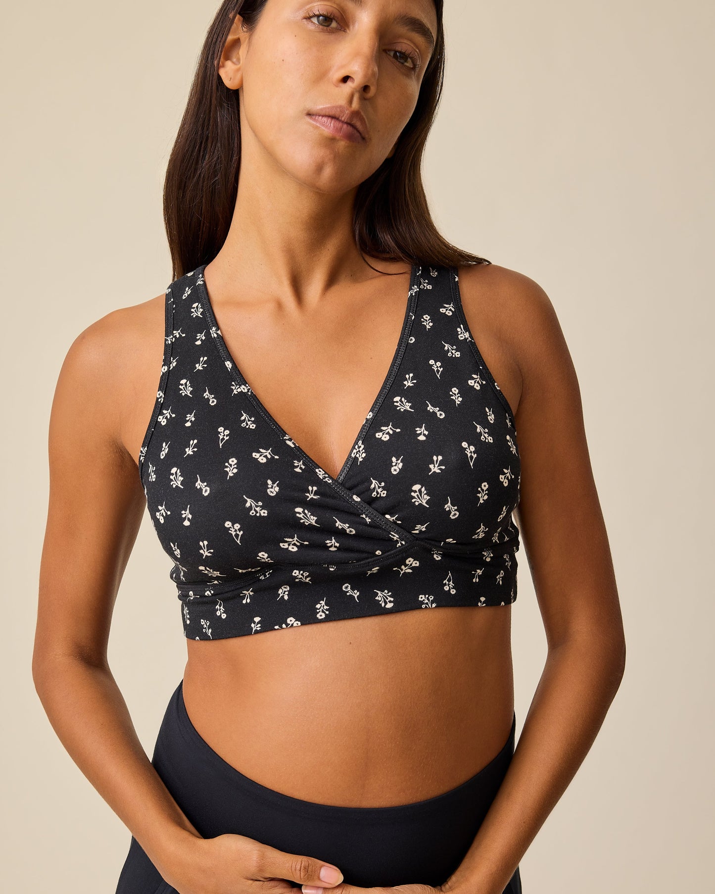 Model is wearing the French Terry Racerback Nursing & Sleep Bra in Black Wildflower pattern on a beige background. @model_info:Hayley is wearing a Small.