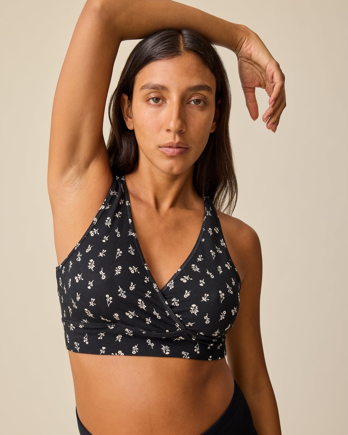 Model is wearing the French Terry Racerback Nursing & Sleep Bra in Black Wildflower pattern on a beige background.