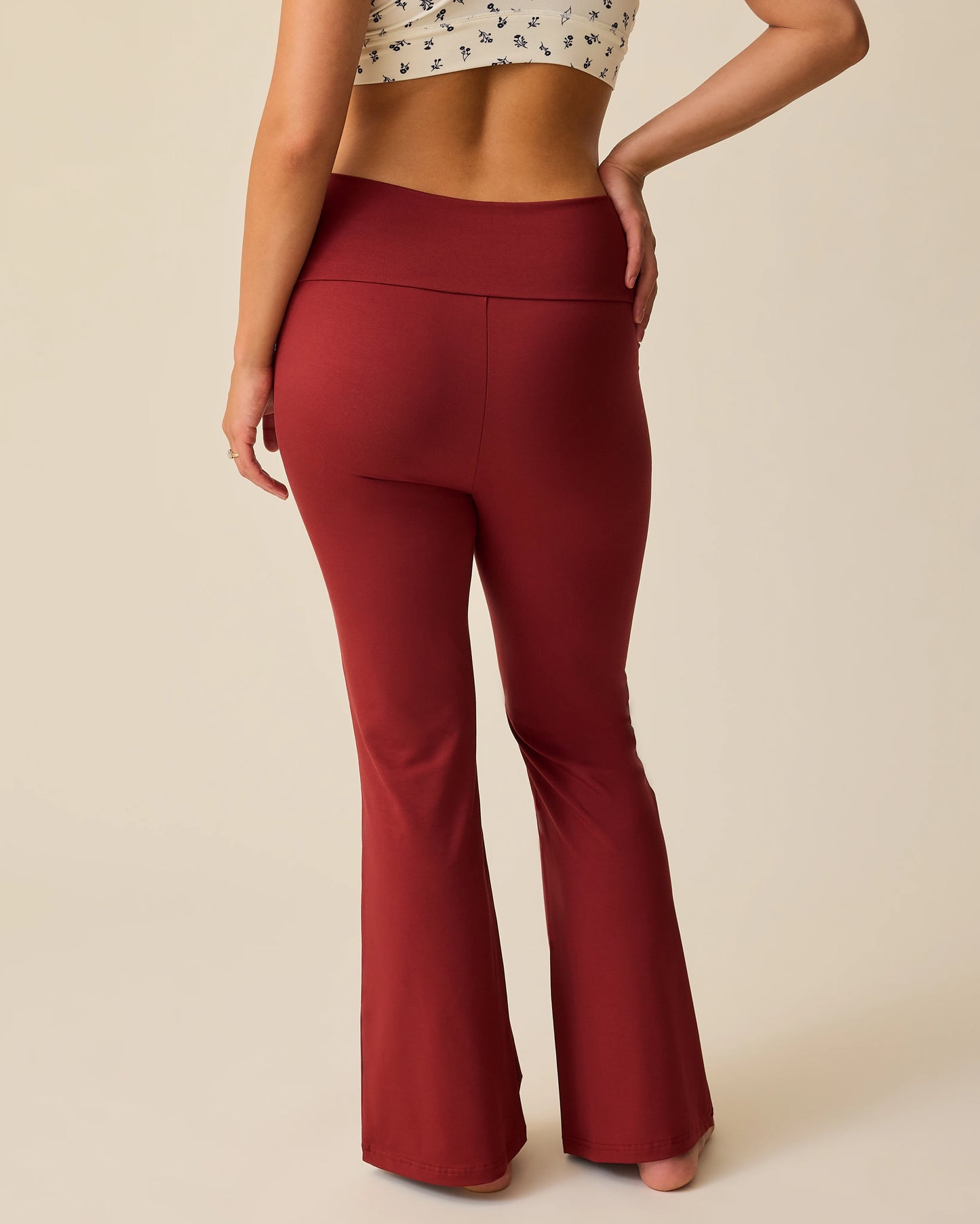 Back view of model wearing French Terry Racerback Nursing & Sleep Bra in Ivory Wildflower and Bamboo Flex Maternity & Postpartum Flare Pant in Auburn on a beige background.