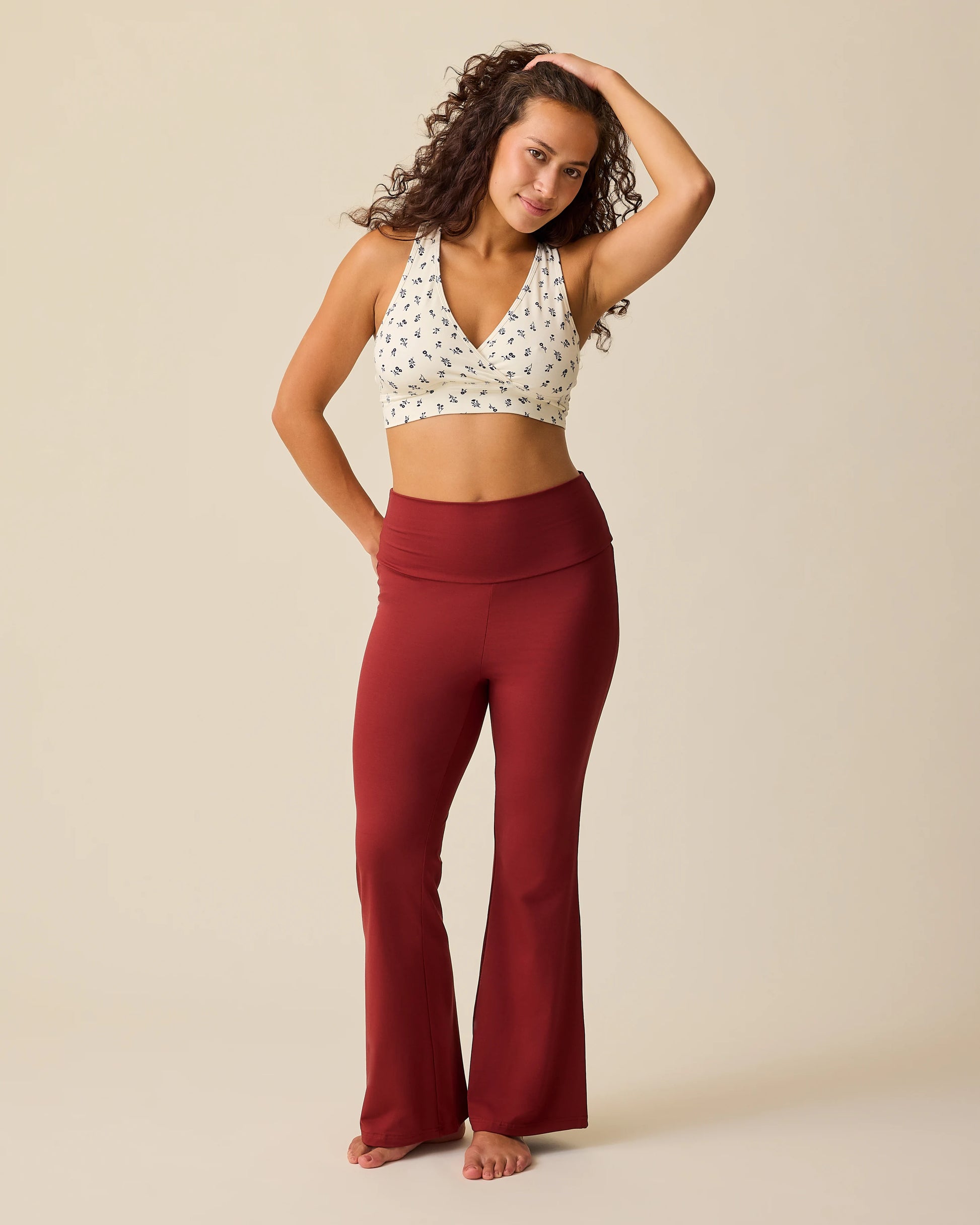 Model is wearing French Terry Racerback Nursing & Sleep Bra in Ivory Wildflower and Bamboo Flex Maternity & Postpartum Flare Pant in Auburn on a beige background.
