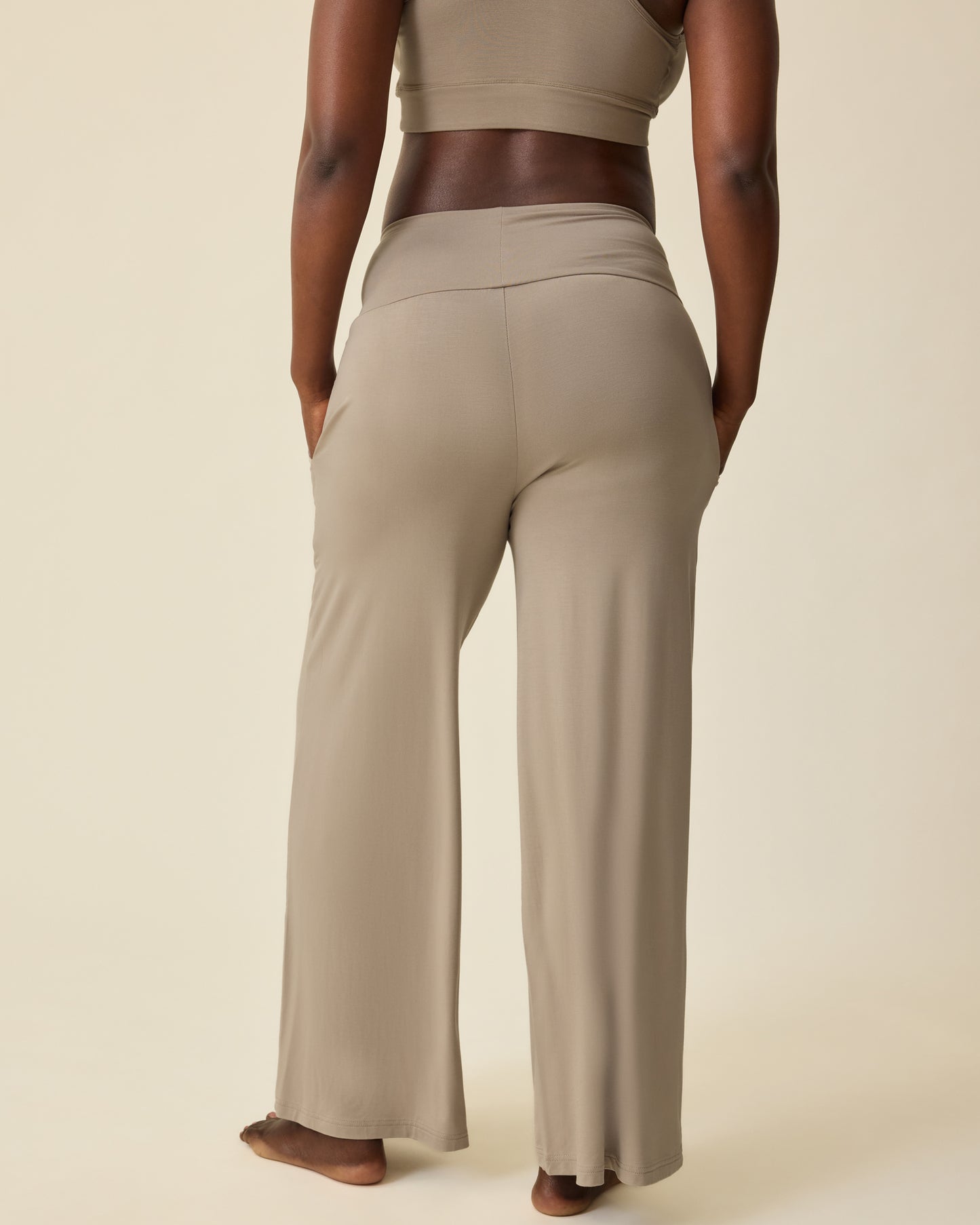 Back view of pregnant model wearing French Terry Racerback Nursing & Sleep Bra in Sandstone and Bamboo Wide Leg Maternity & Postpartum Lounge Pant in Sandstone on a beige background.