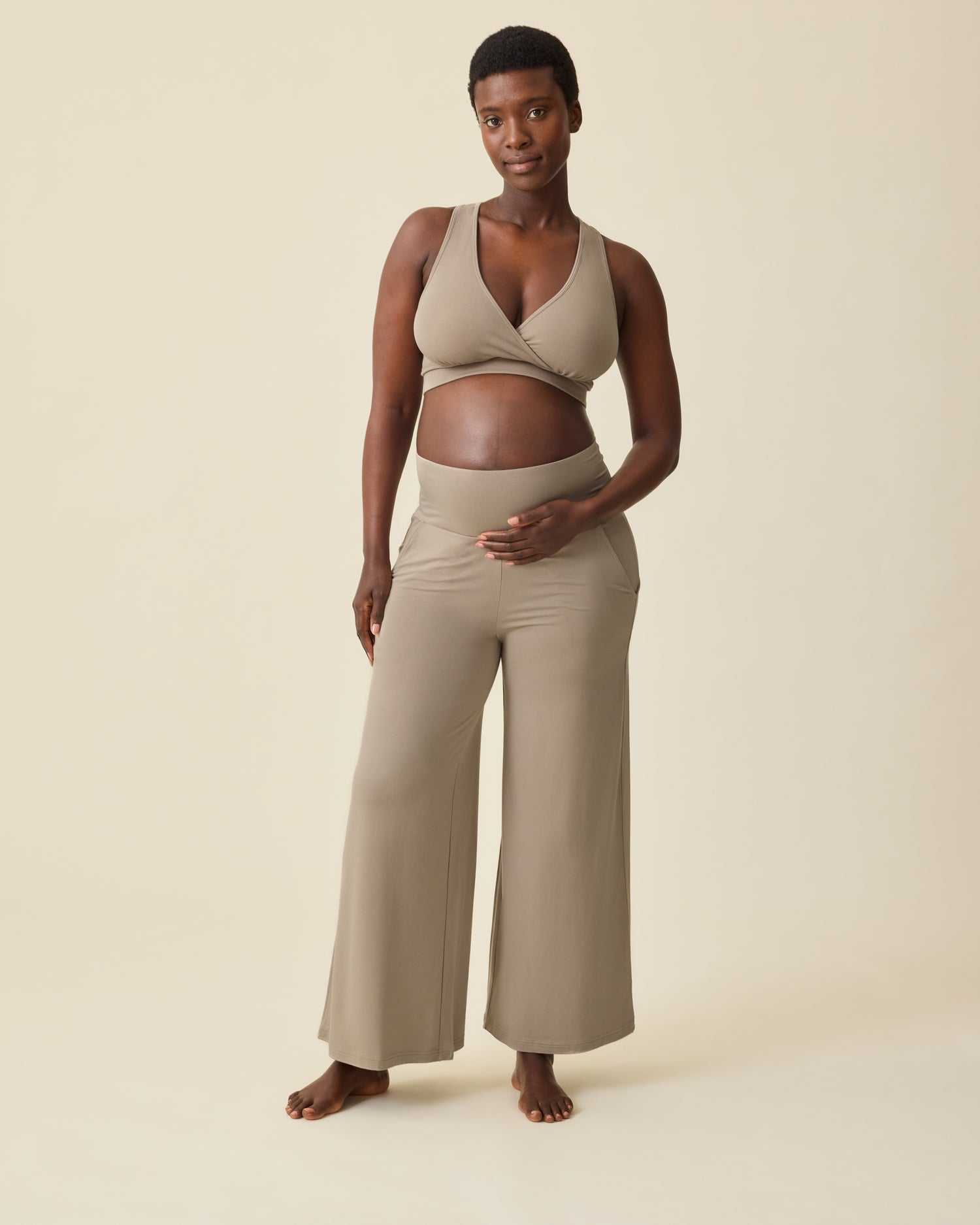 Pregnant model is wearing French Terry Racerback Nursing & Sleep Bra in Sandstone and Bamboo Wide Leg Maternity & Postpartum Lounge Pant in Sandstone on a beige background. @model_info:Anna is 5'8.5" and wearing a Medium.