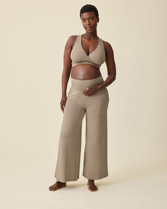 Pregnant model is wearing French Terry Racerback Nursing & Sleep Bra in Sandstone and Bamboo Wide Leg Maternity & Postpartum Lounge Pant in Sandstone on a beige background. @model_info:Anna is 5'8.5" and wearing a Medium.