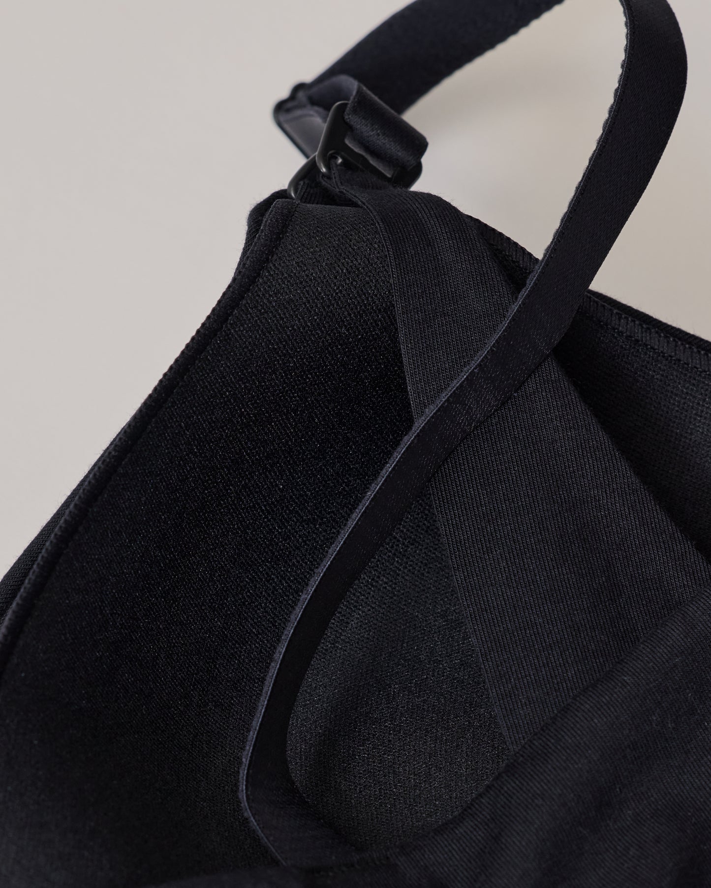 The back view of SoftStretch Cotton Nursing Bra in Black, laying on surface. Soft material and color, support straps and nursing clasps. On a beige background.