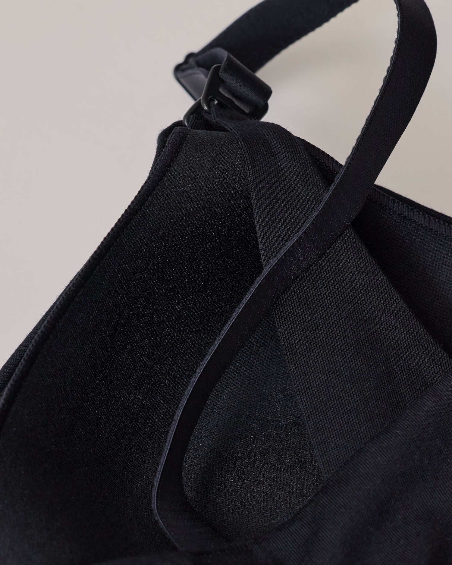 The back view of SoftStretch Cotton Nursing Bra in Black, laying on surface. Soft material and color, support straps and nursing clasps. On a beige background.