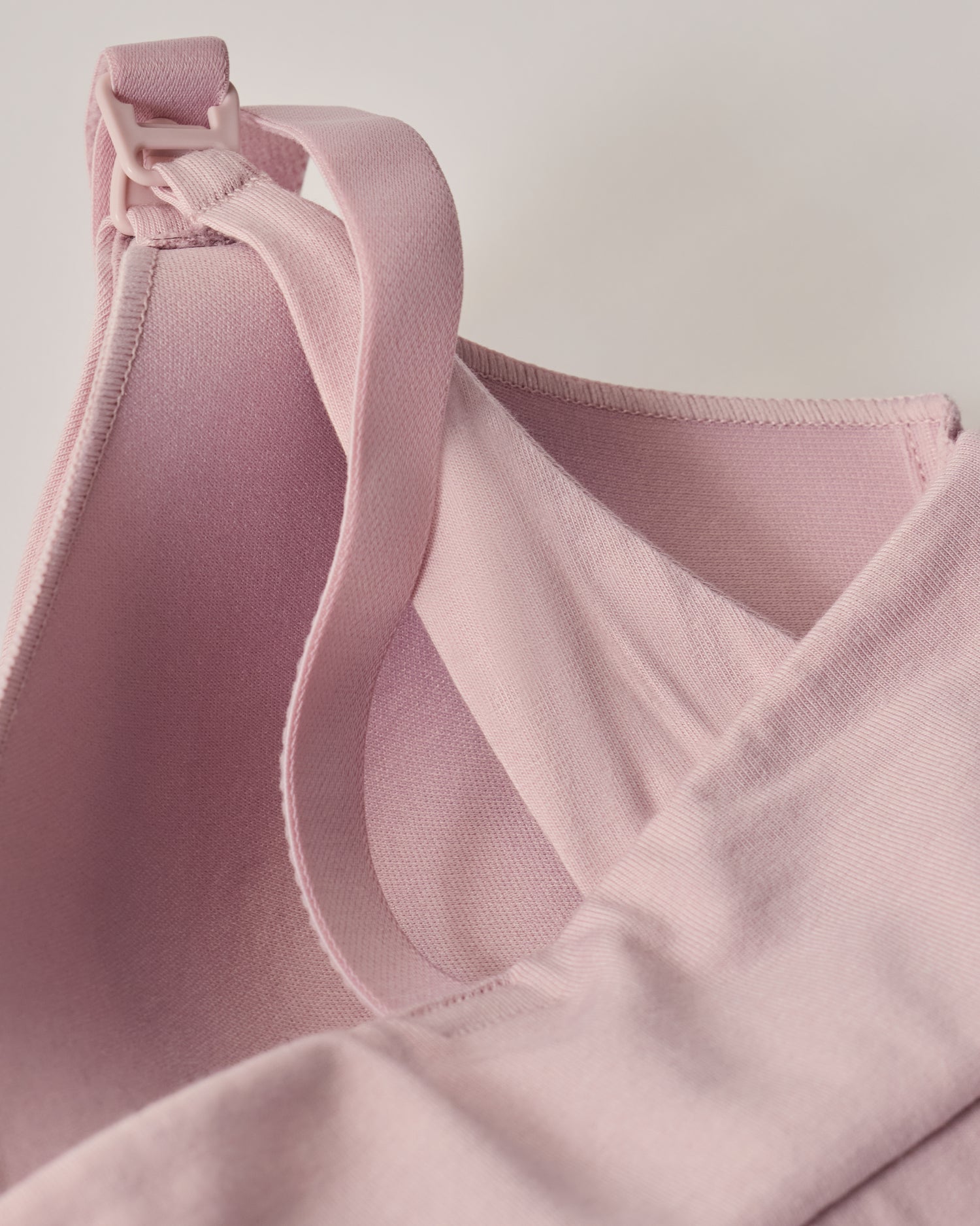 The back view of SoftStretch Cotton Nursing Bra in Lilac Mist, laying on surface. Soft material and color, support straps and nursing clasps. On a beige background.
