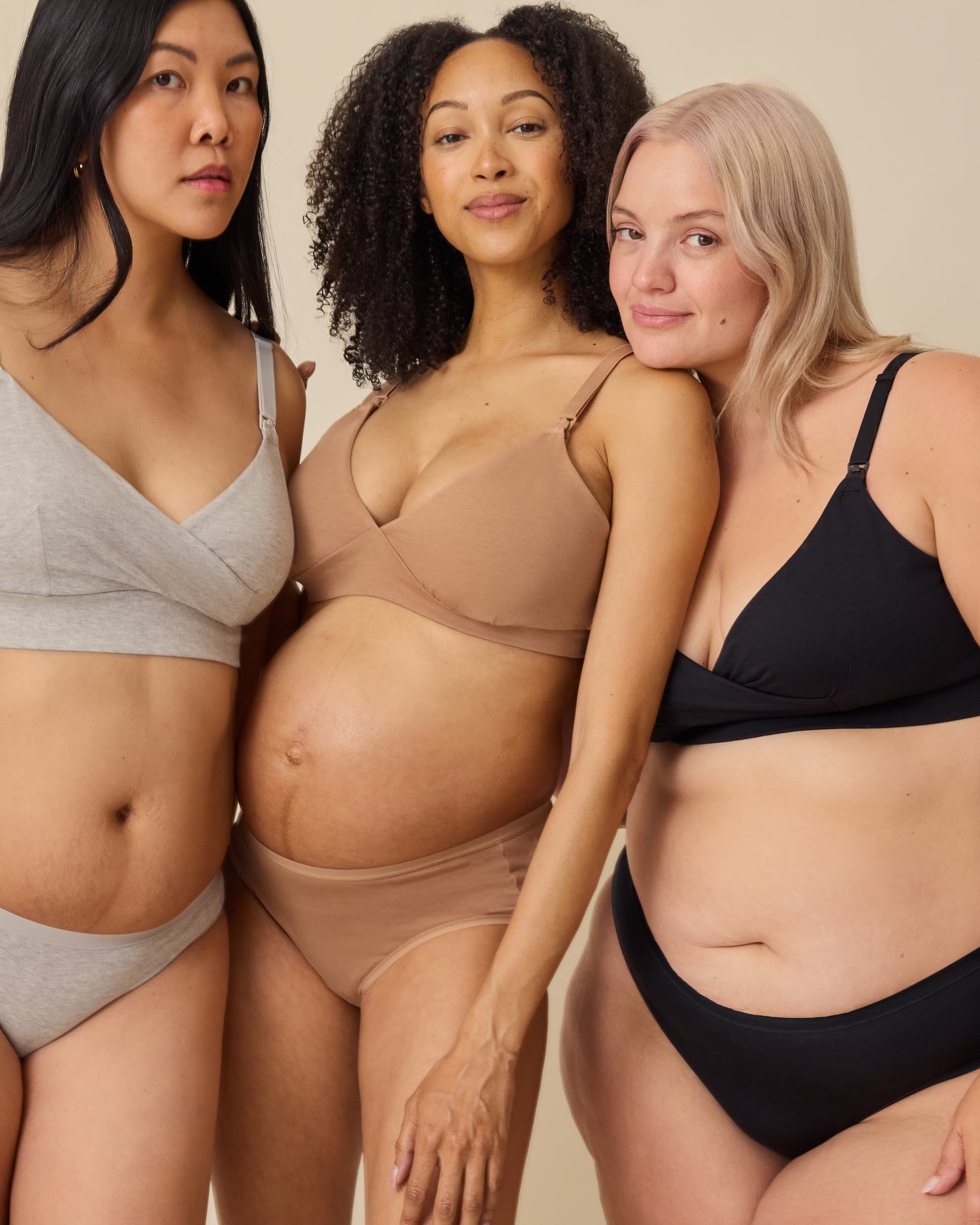 Postpartum model on the left is wearing SoftStretch Cotton Nursing Bra and SoftStretch Cotton Maternity & Postpartum Hipster in Grey Heather. Pregnant model in the middle is wearing SoftStretch Cotton Maternity & Nursing Bralette and SoftStretch Cotton Maternity & Postpartum Brief in Buff. Model on right is wearing SoftStretch Cotton Nursing Bra and SoftStretch Cotton Maternity & Postpartum Hipster in Black on a beige background. 