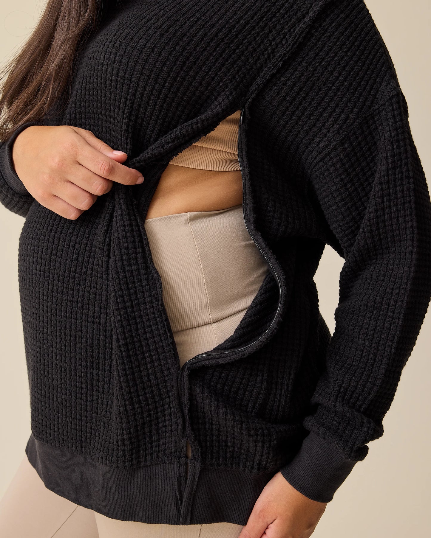 Model is showing the zipper opening for nursing access on the Joelle Thermal Maternity & Nursing Top in Black on a beige background.