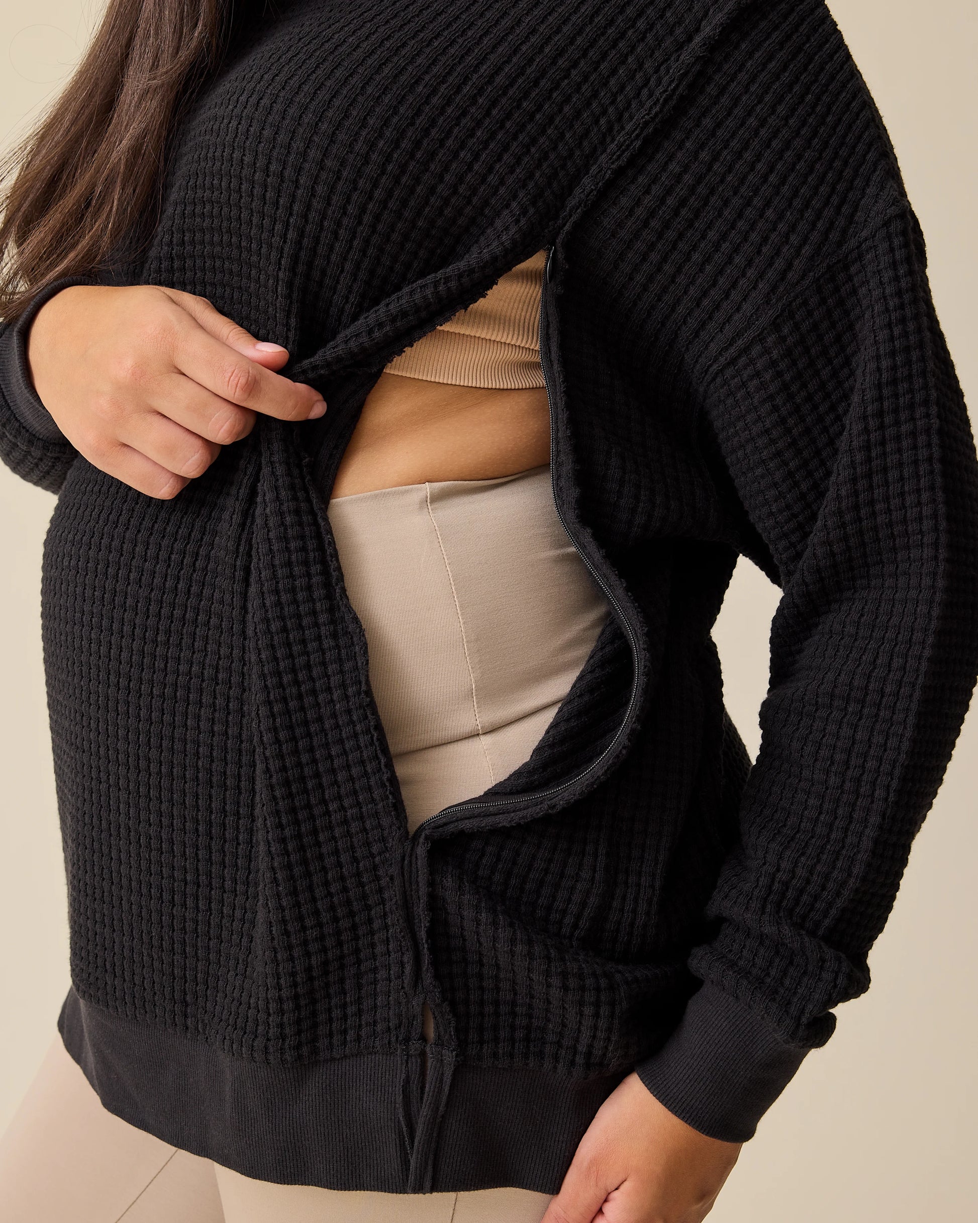 Model is showing the zipper opening for nursing access on the Joelle Thermal Maternity & Nursing Top in Black on a beige background.