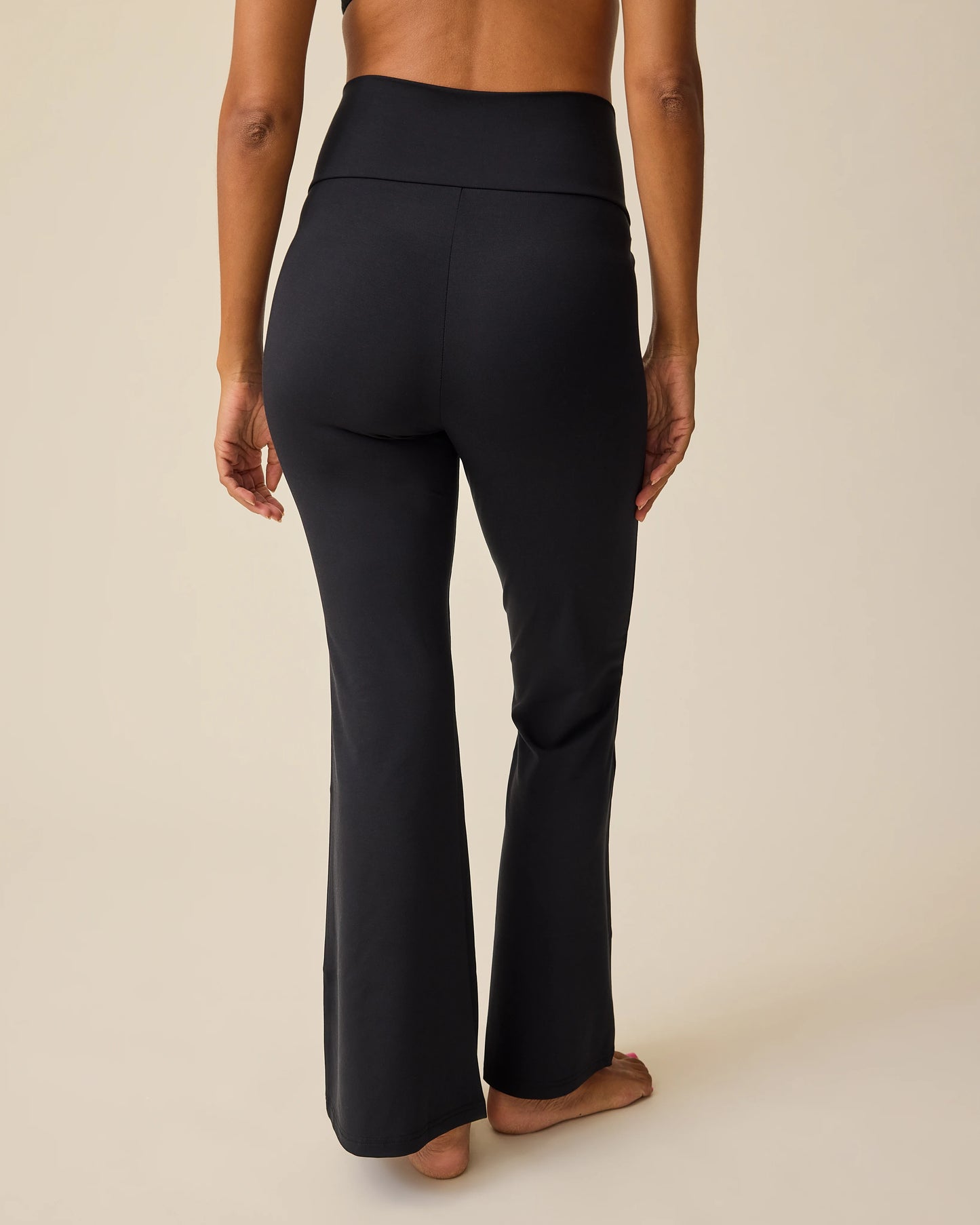 Back view of model wearing Bamboo Flex Maternity & Postpartum Flare Pant in Black on a beige background.