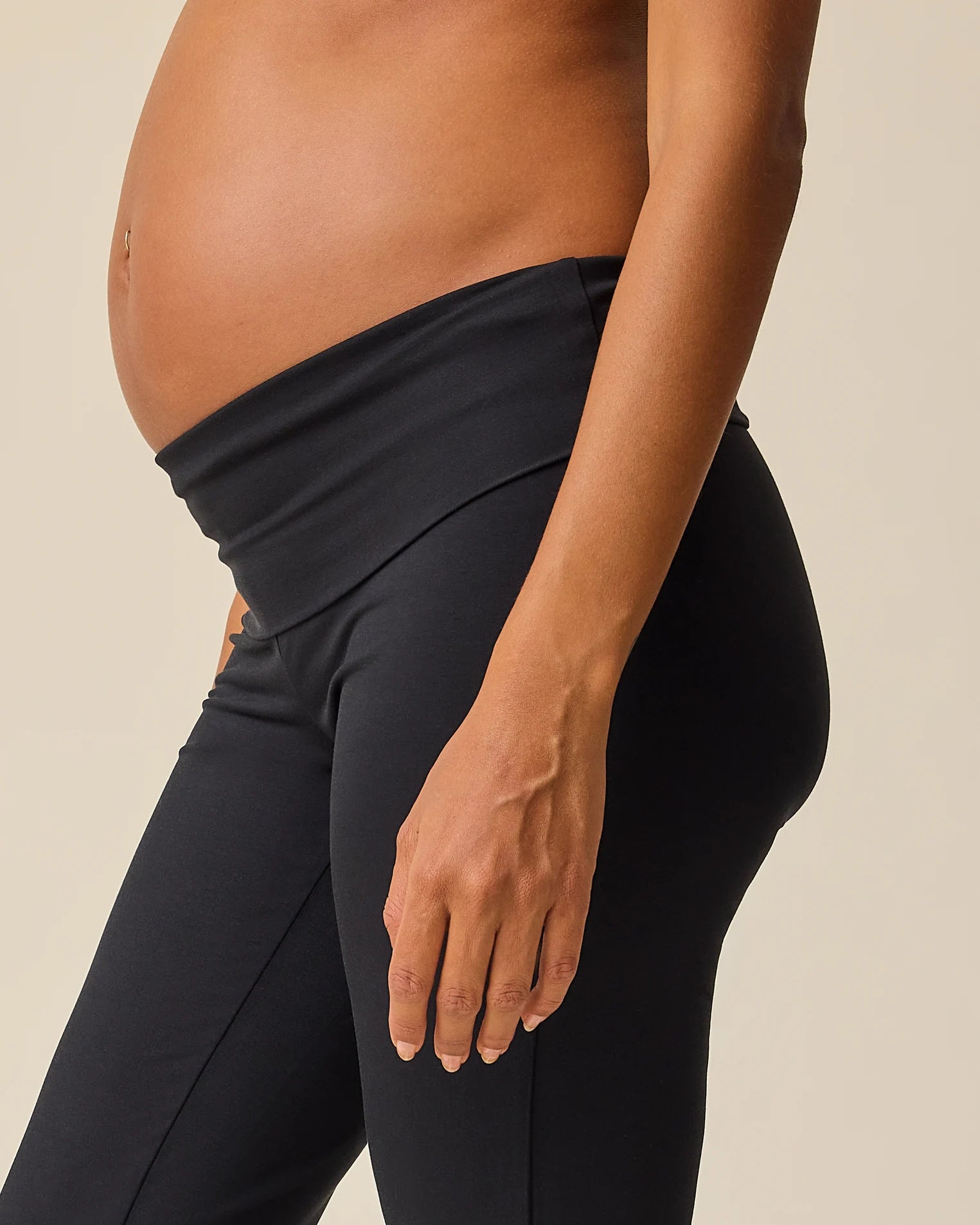 Close up of model wearing Bamboo Flex Maternity & Postpartum Flare Pant in Black on a beige background.