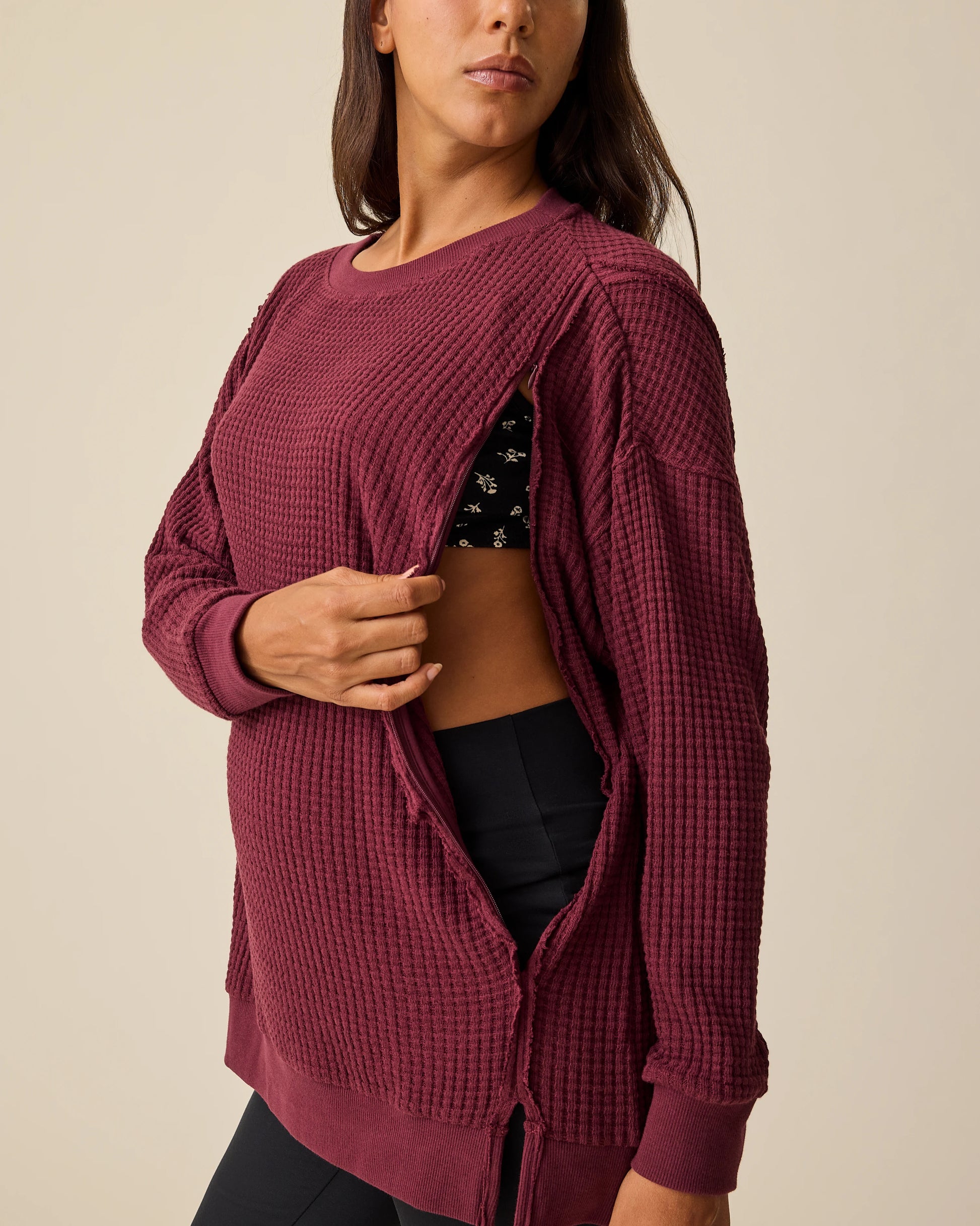 Model is displaying easy nursing access  zipper on the Joelle Thermal Maternity & Nursing Top in Garnet with black pants on a beige background.