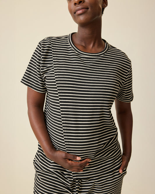 Model is wearing Luxe Terry Maternity & Nursing Split Hem T-shirt in Black & Ivory Stripe and Luxe Terry Maternity & Postpartum Pant in Black & Ivory Stripe, on a beige background.@model_info:Anna is wearing a Small.