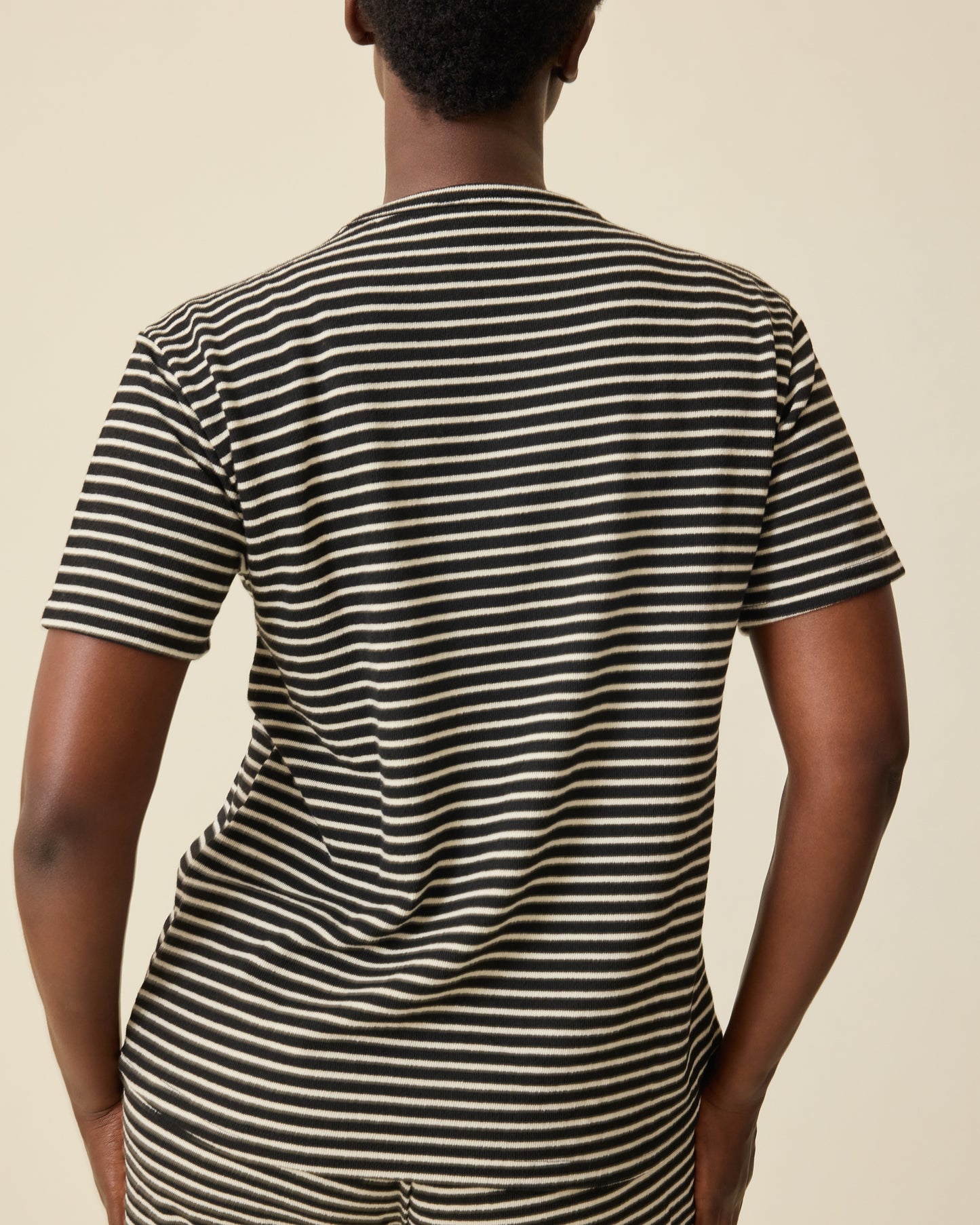 Back view of model wearing Luxe Terry Maternity & Nursing Split Hem T-shirt in Black & Ivory Stripe and Luxe Terry Maternity & Postpartum Pant in Black & Ivory Stripe, on a beige background.