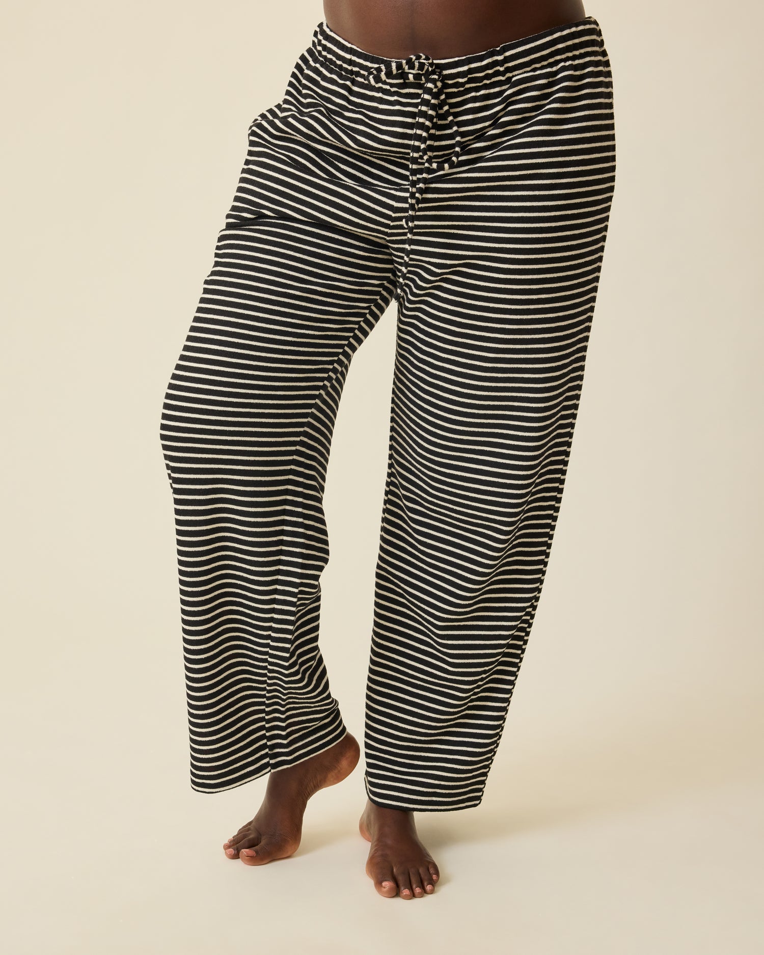 Model is wearing Luxe Terry Maternity & Postpartum Pant in Black & Ivory Stripe, on a beige background.@model_info:Anna is 5'8.5" and wearing a Large.