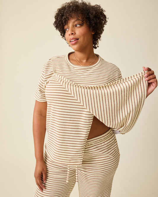 Model is lifting up the breastfeeding flap for access on  Luxe Terry Maternity & Nursing Split Hem T-shirt in Ivory & Chocolate Stripe and Luxe Terry Maternity & Postpartum Pant in Ivory & Chocolate Stripe, on a beige background.@model_info:Skye is wearing an X-Large.