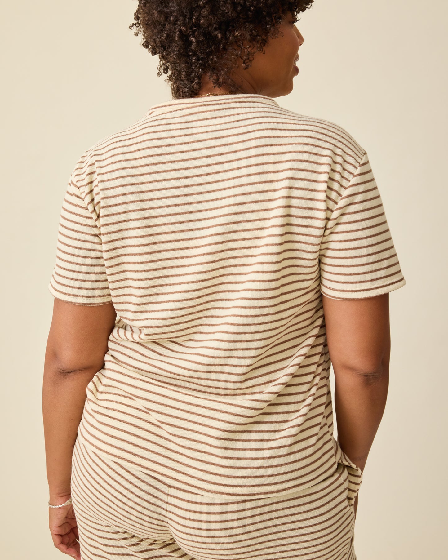 Back view on the Luxe Terry Maternity & Nursing Split Hem T-shirt in Ivory & Chocolate Stripe and Luxe Terry Maternity & Postpartum Pant in Ivory & Chocolate Stripe, on a beige background.